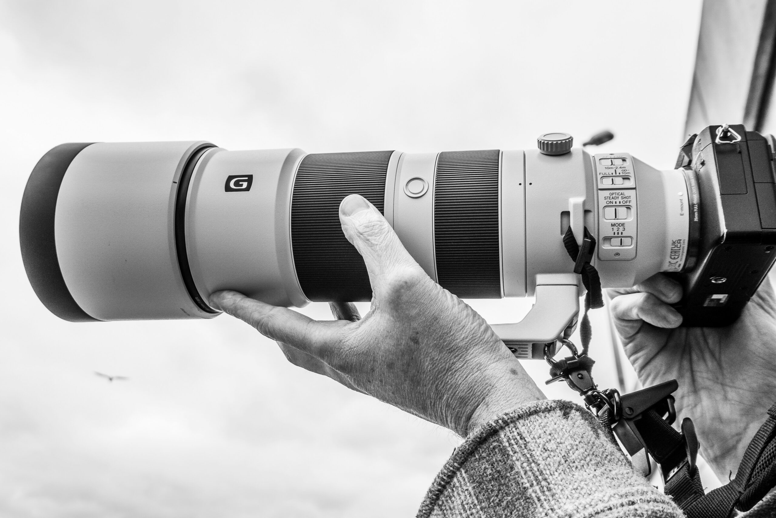Photographer handholding a camera and telephoto lens for aviation photography at an airshow