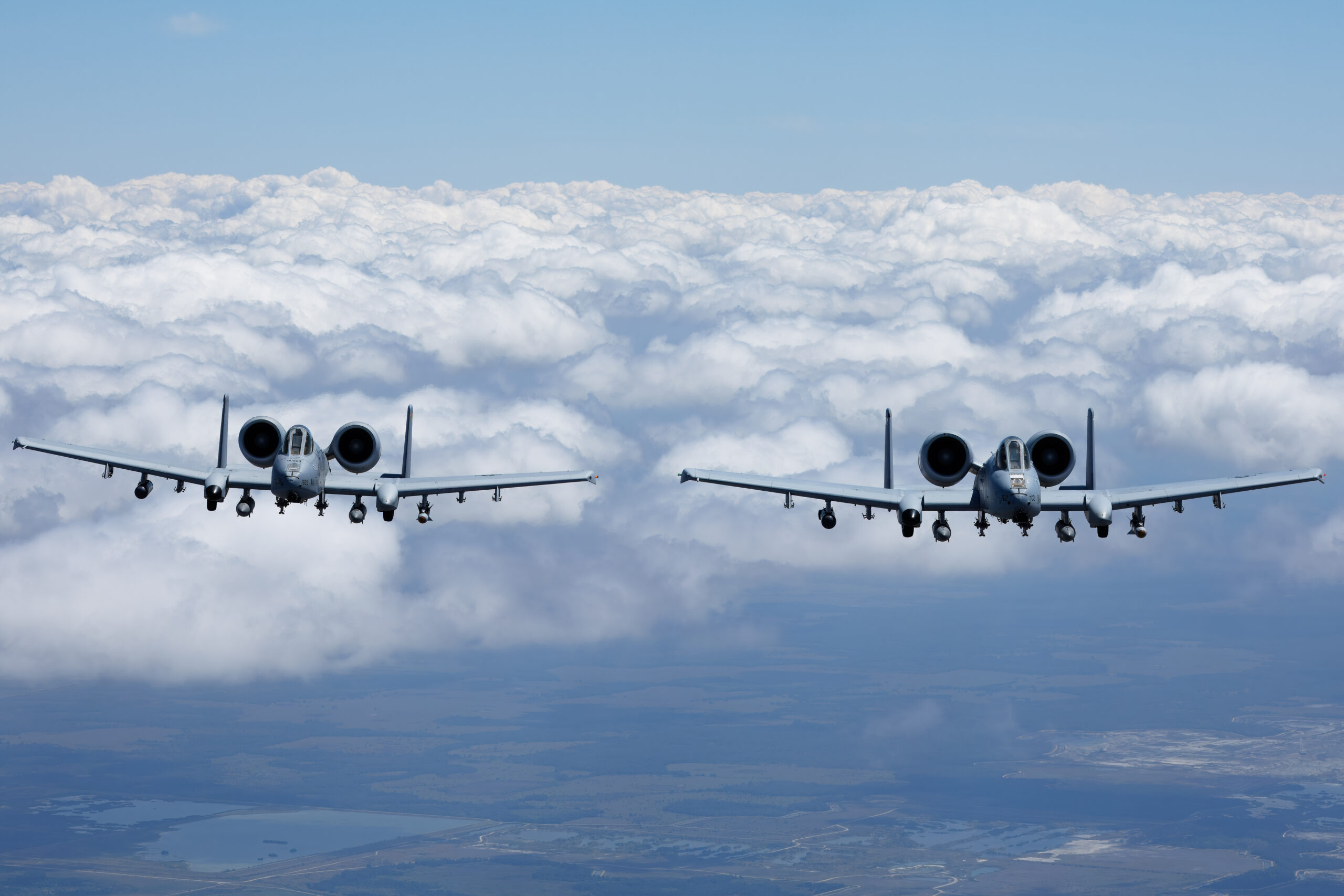 A pair of A-10C Thunderbolt IIs side by side above a cloud deck