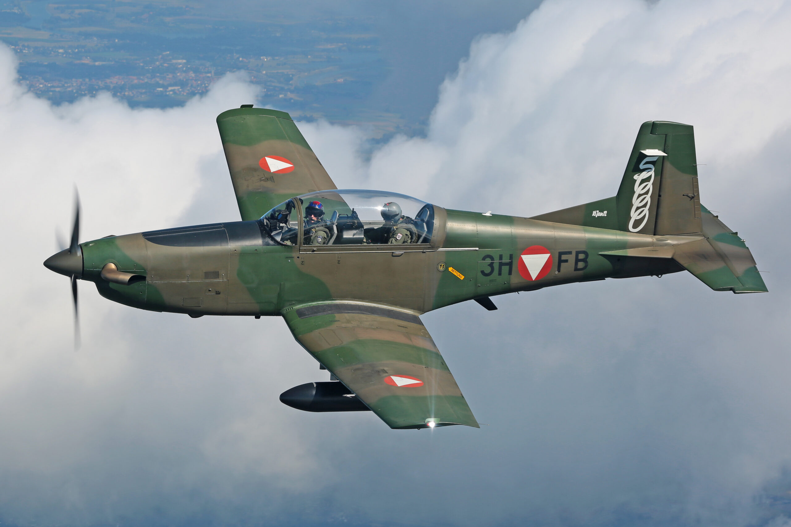 Austrian Air Force Pilatus PC-7 trainer 3H-FB in green camouflage, side-on above a bank of cloud, propeller blurred