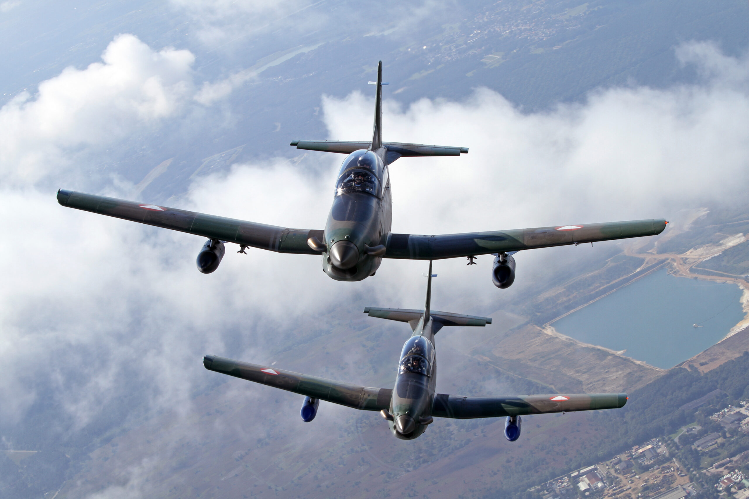 Two Austrian Air Force Pilatus PC-7 trainers stacked in close formation above clouds