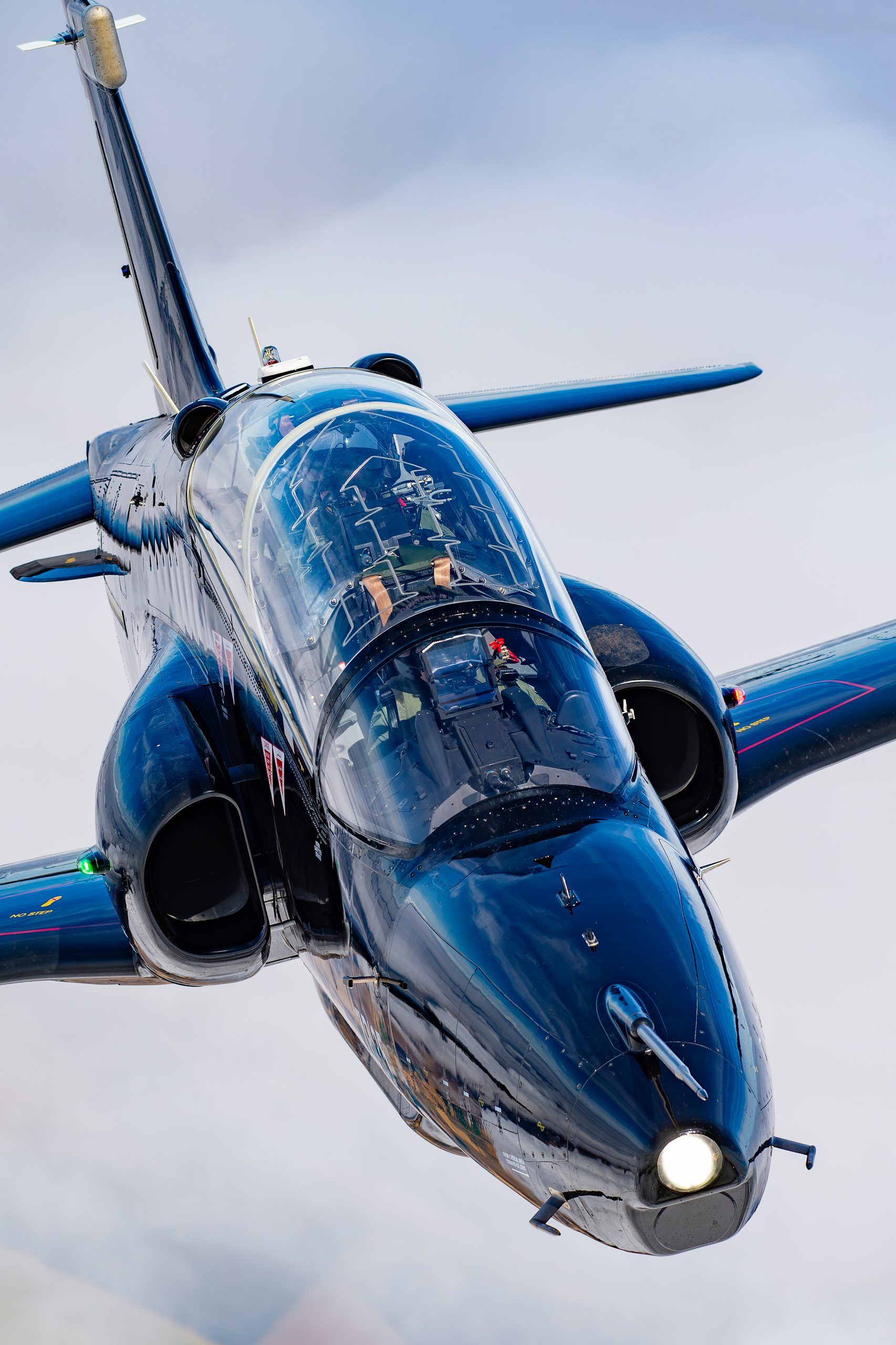 A BAE Systems Hawk in a dark blue scheme banks towards the camera on an air-to-air sortie