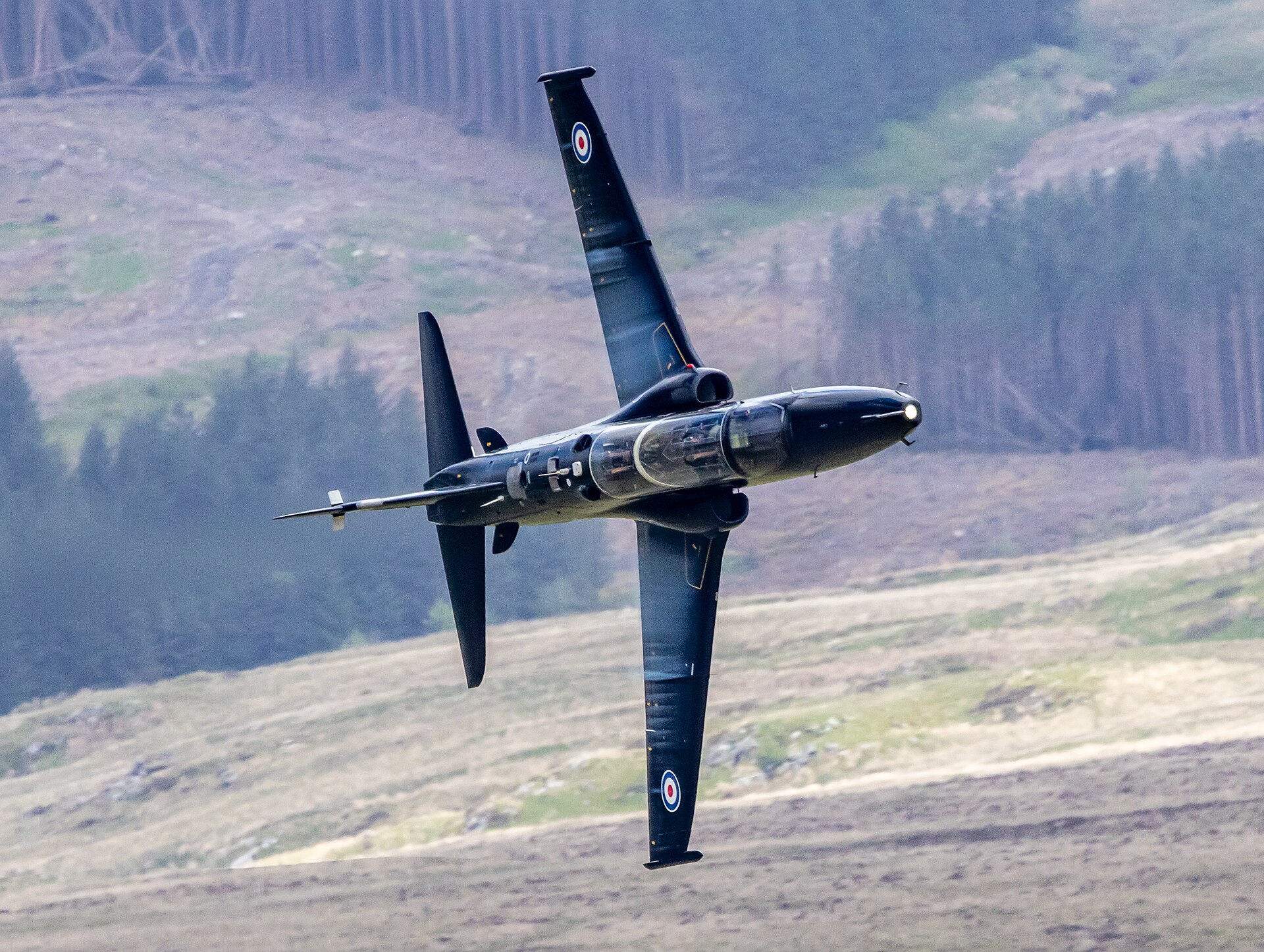 RAF BAE Hawk banking hard past Cad West in the Mach Loop, seen from above against the valley floor