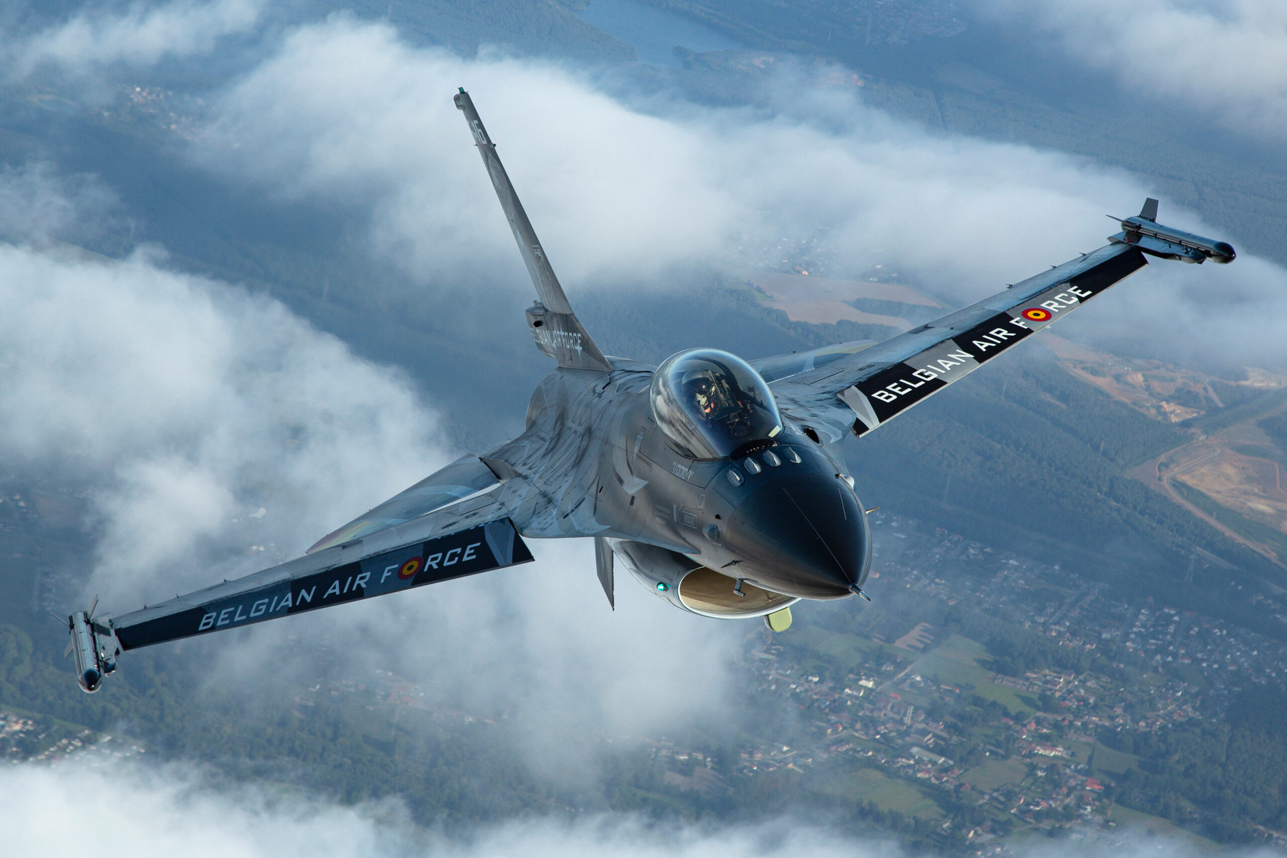 Belgian Air Force F-16AM banking above broken cloud, with BELGIAN AIR FORCE titles under both wings