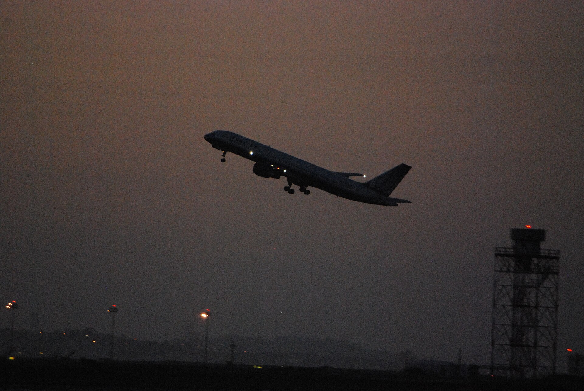Boeing 757 lifting off after dusk with landing lights blazing against a dark sky