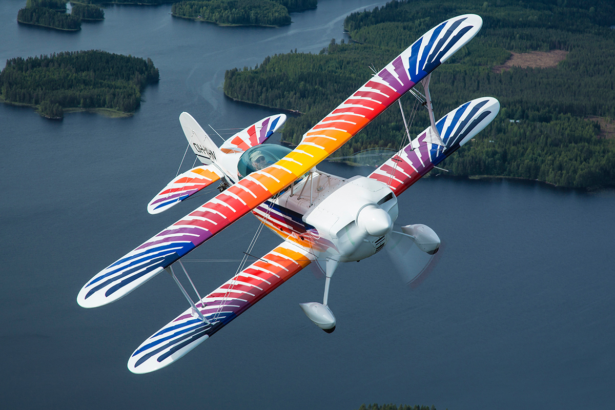 Colourful Christen Eagle II biplane banking over lakes and forest