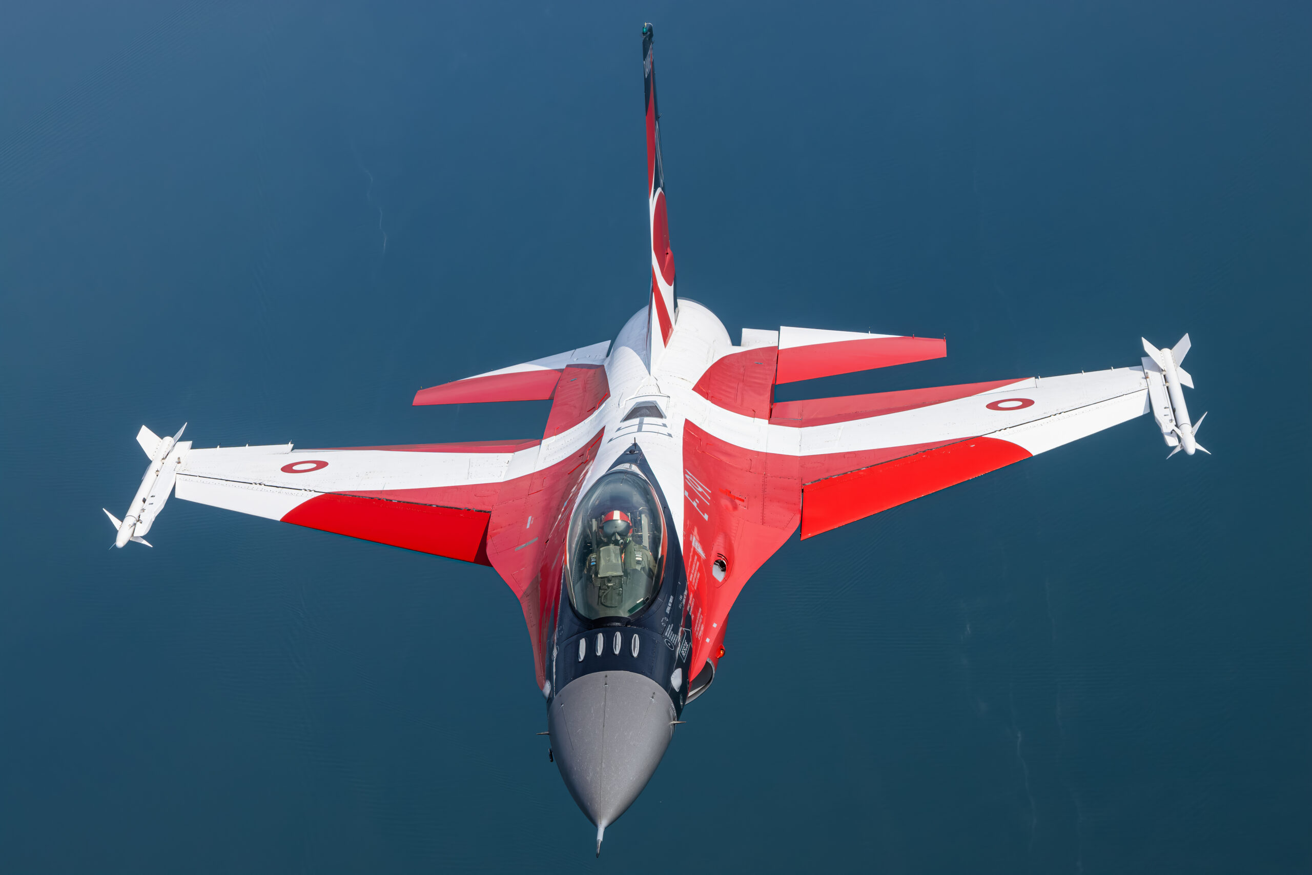 Royal Danish Air Force F-16AM E-191 in red and white Dannebrog special scheme seen from above over dark water