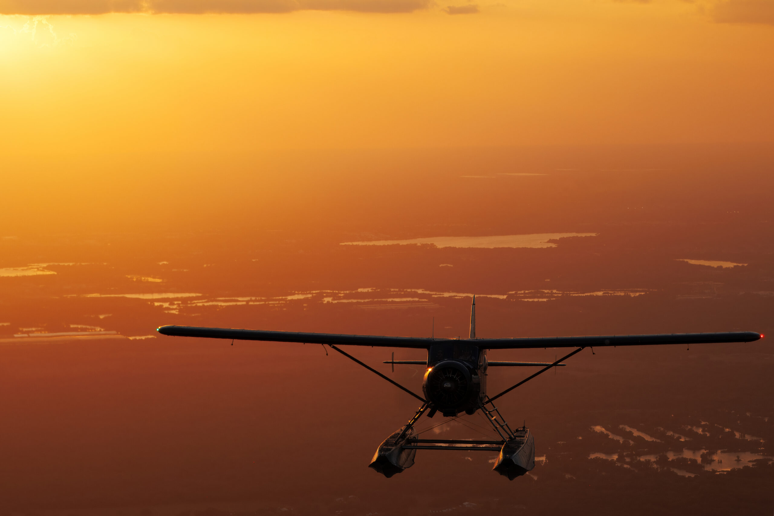 DHC-2 Beaver floatplane head-on, silhouetted against orange dusk