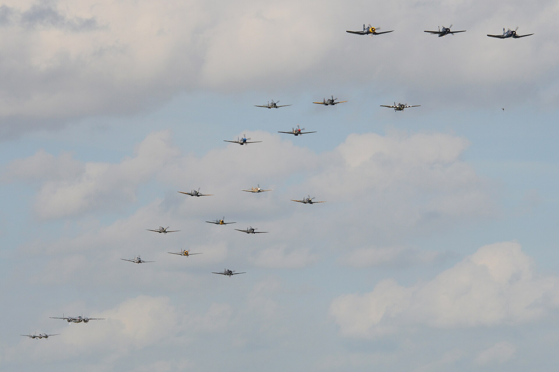 Large formation of piston warbirds flying together over Duxford airfield