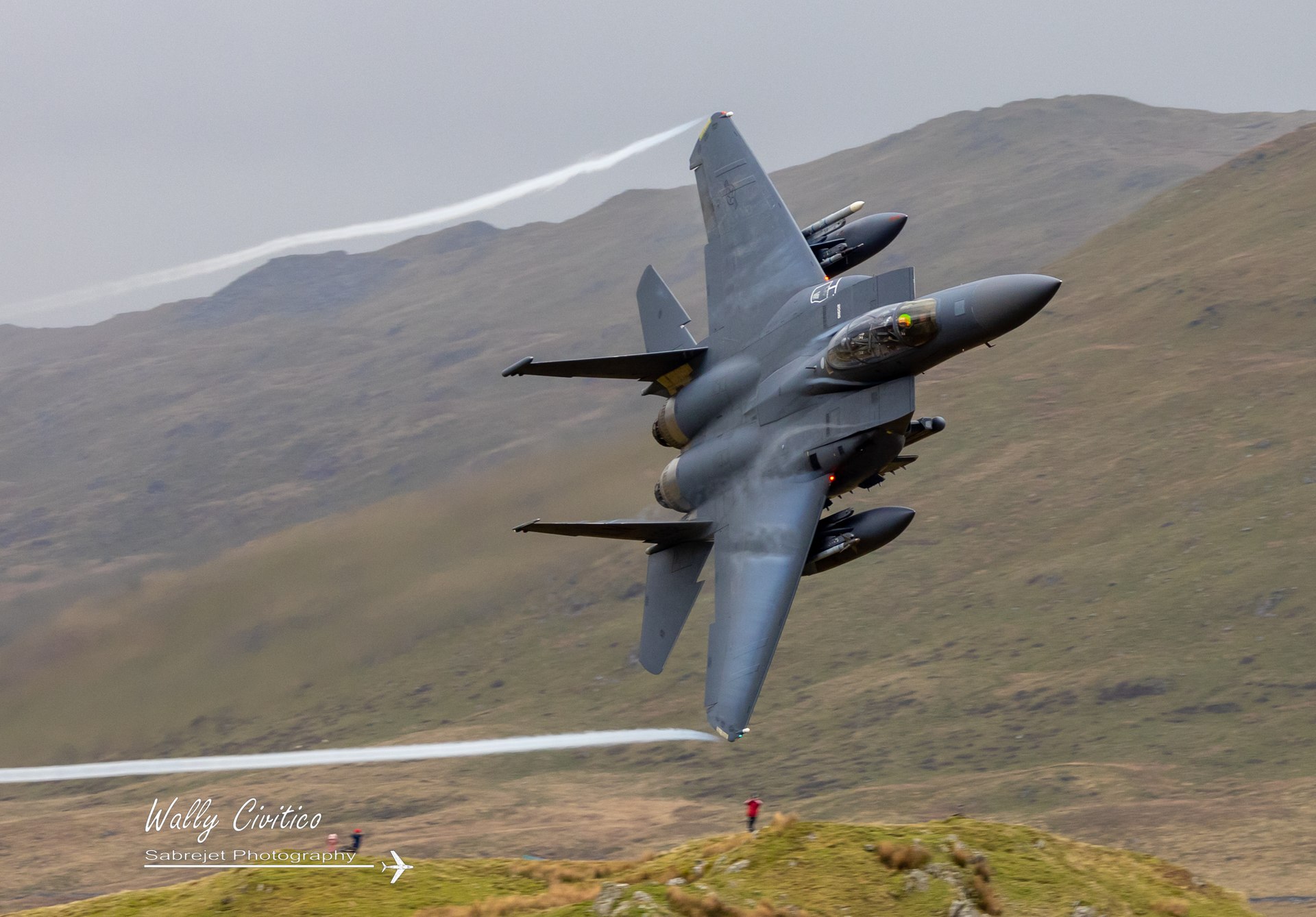 Topside view of a USAF F-15E Strike Eagle pulling vapour vortices below Cad West in the Mach Loop