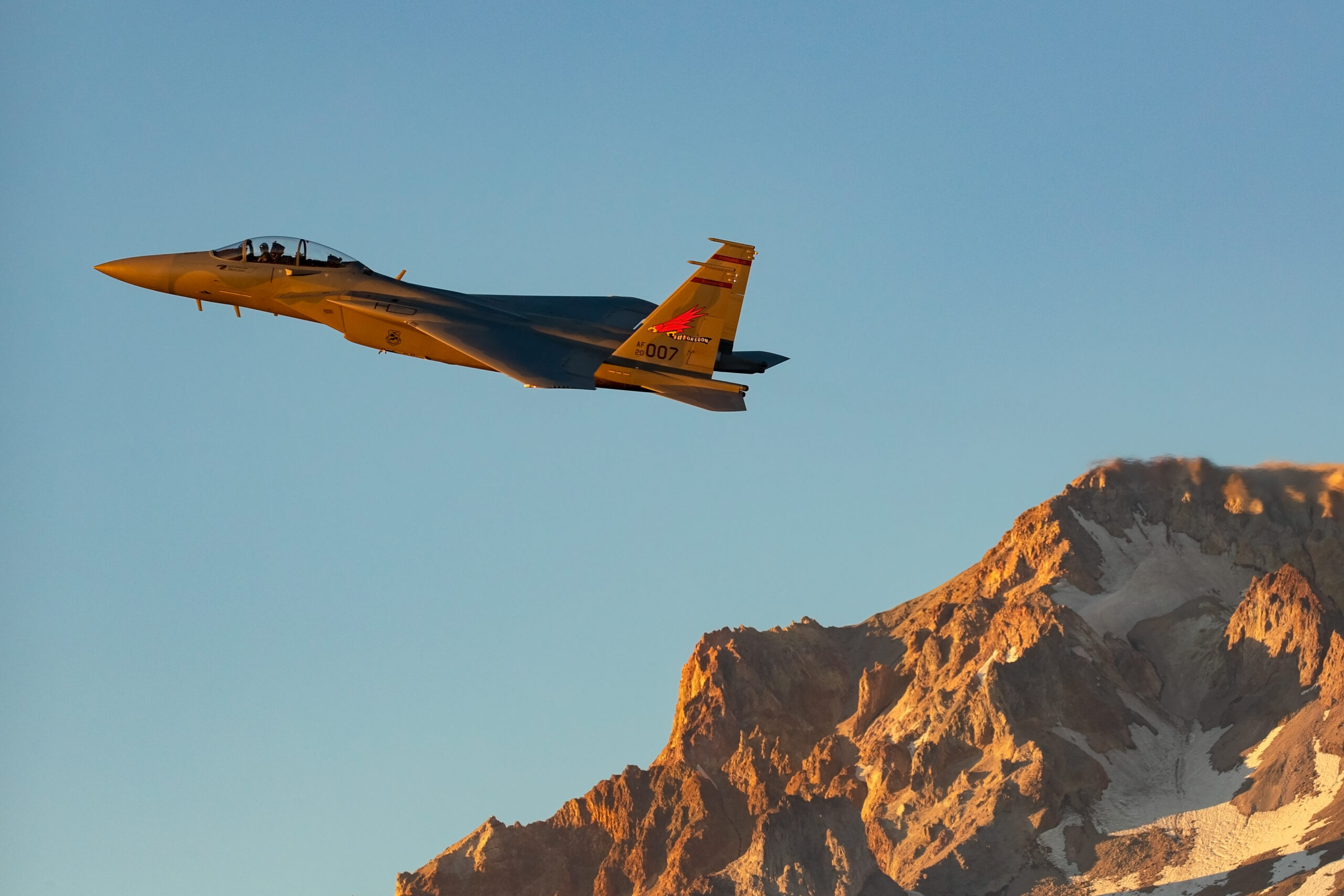 F-15EX Eagle II of the 142nd Wing banking over a mountain peak in golden light