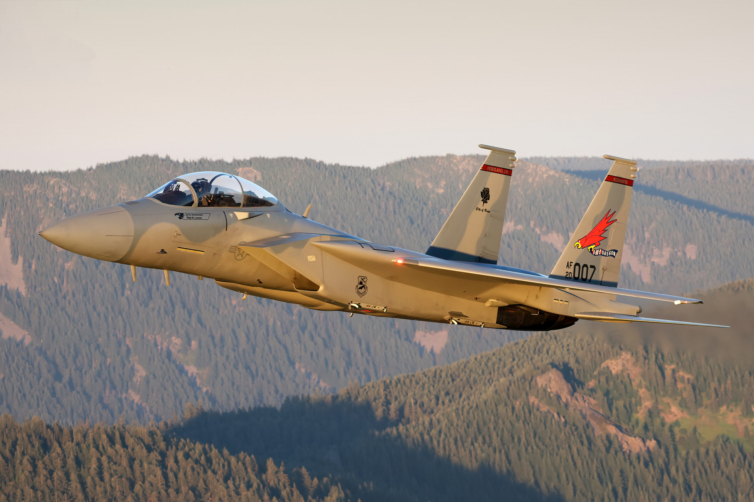 F-15EX Eagle II of the Oregon ANG Redhawks in warm golden-hour light over forested ridges