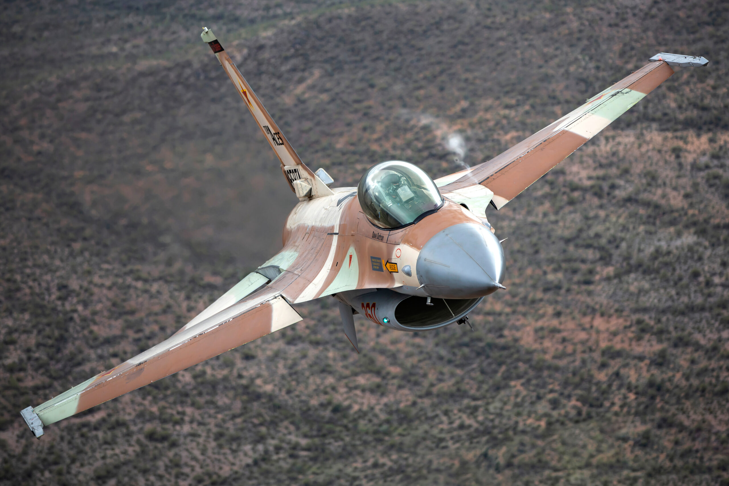 F-16A Netz in brown and tan desert camouflage banking head-on over a desert hillside