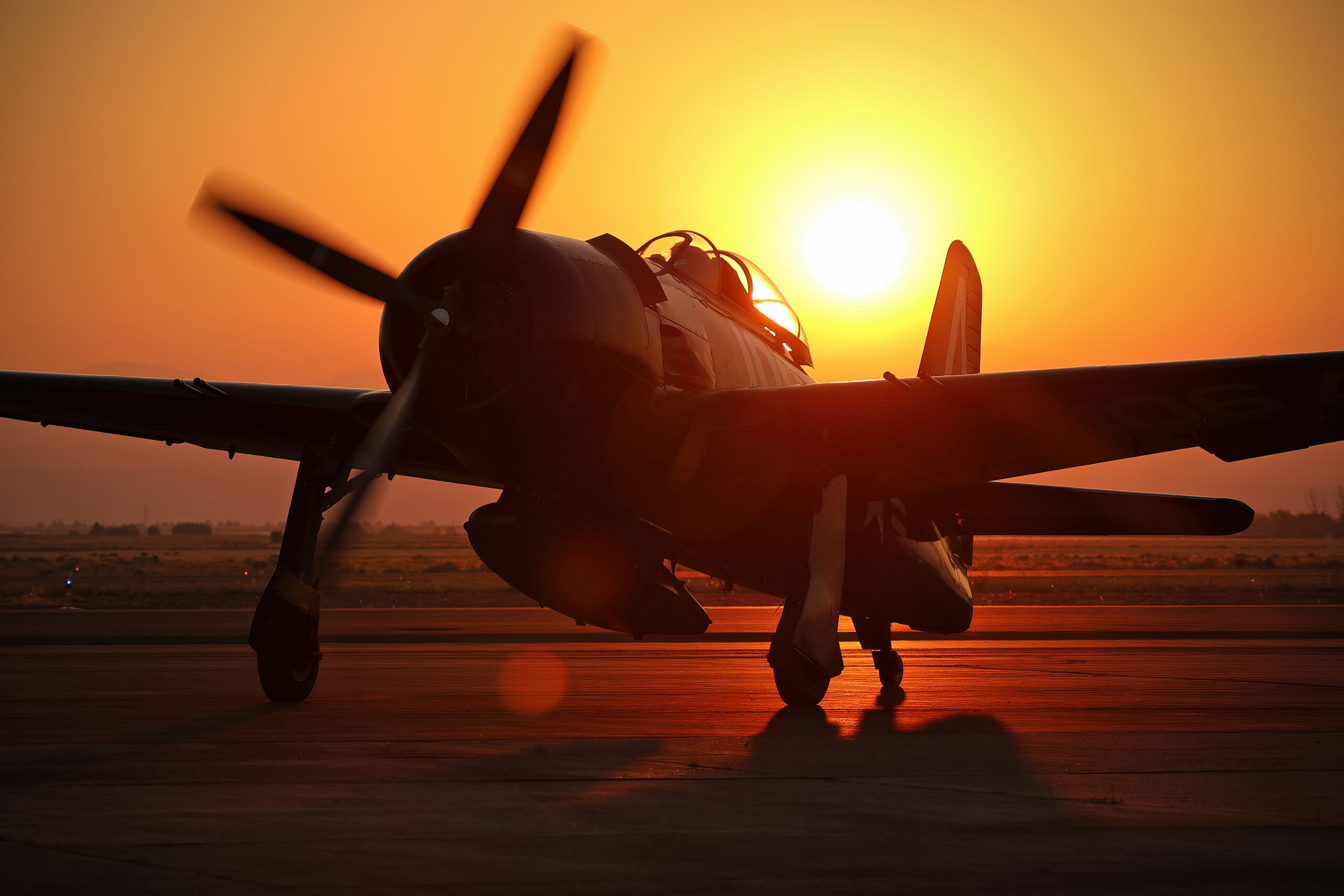 Grumman F8F Bearcat running up at sunset, silhouetted with lens flare