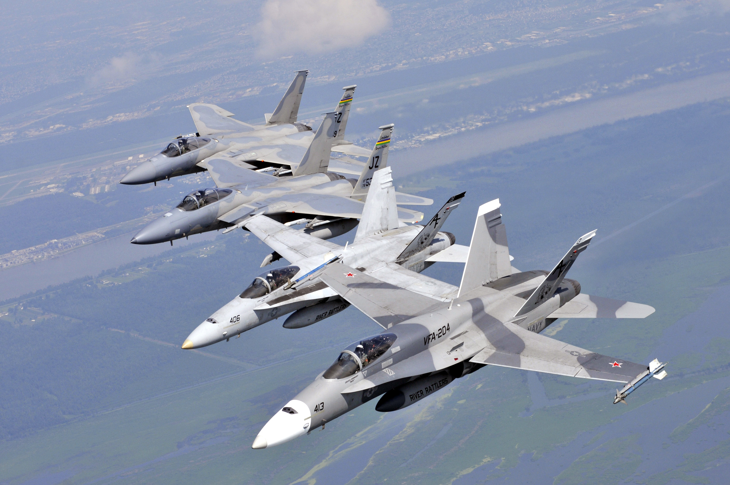 Two F/A-18 Hornets and two F-15 Strike Eagles flying in echelon formation, photographed from another aircraft
