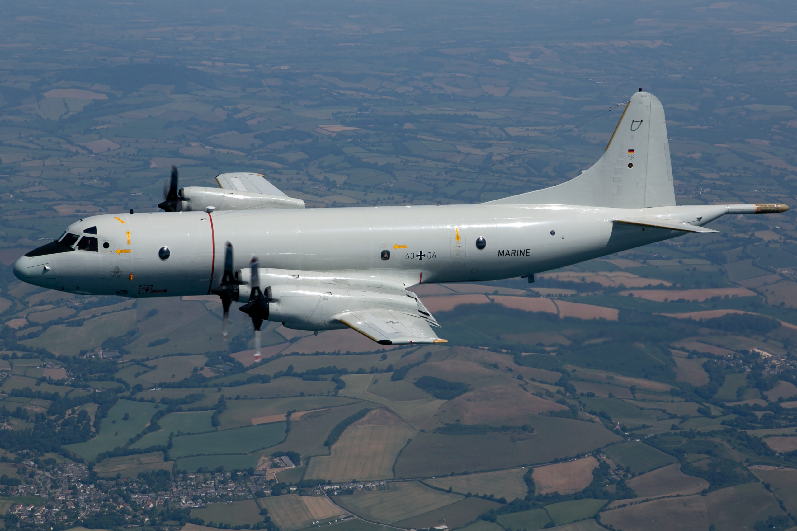 German Navy P-3C Orion 60+06 in level side profile over patchwork fields, all four propellers blurred