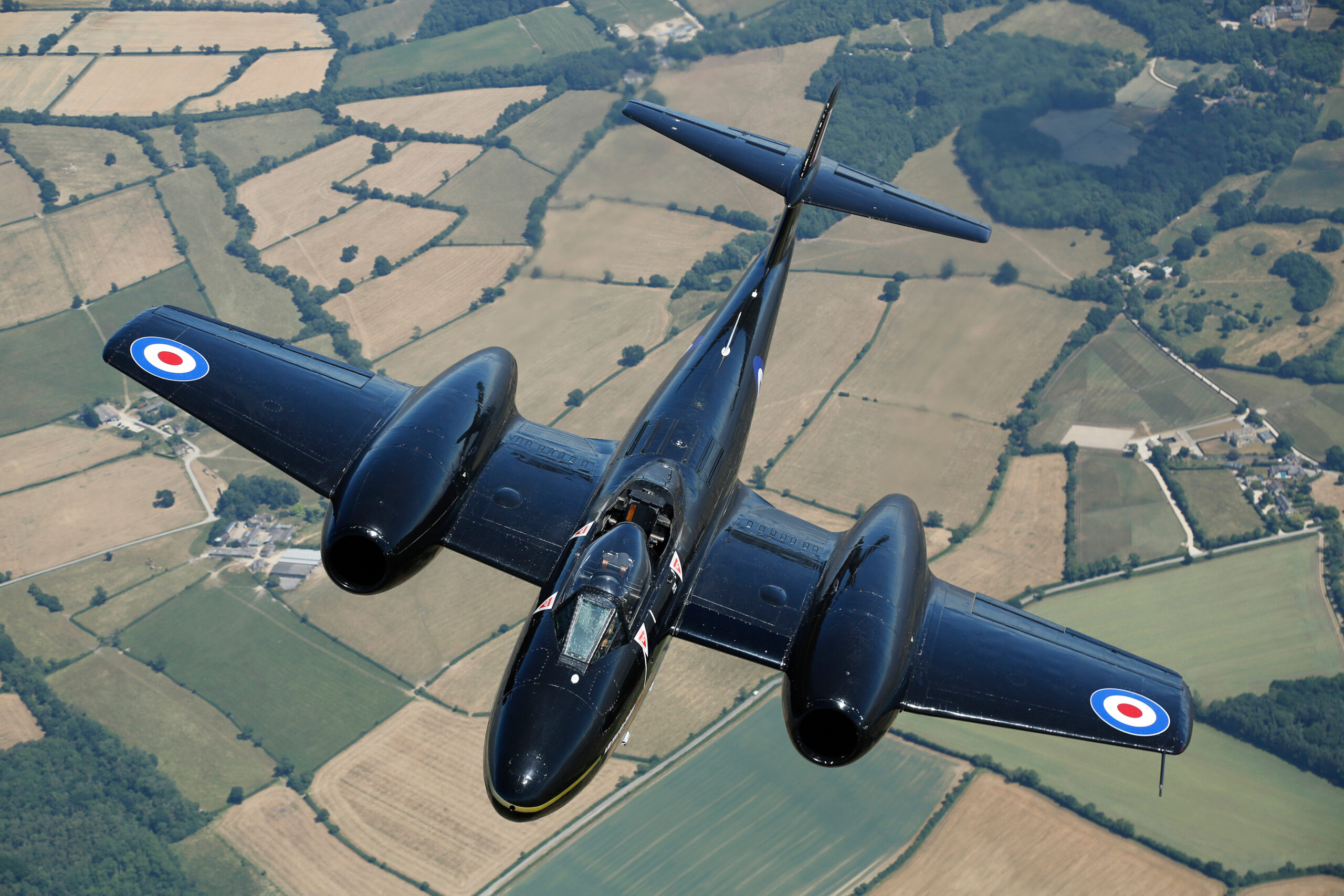 Black-painted Gloster Meteor T7 WA638 banking over English fields, seen from above with RAF roundels on the wings