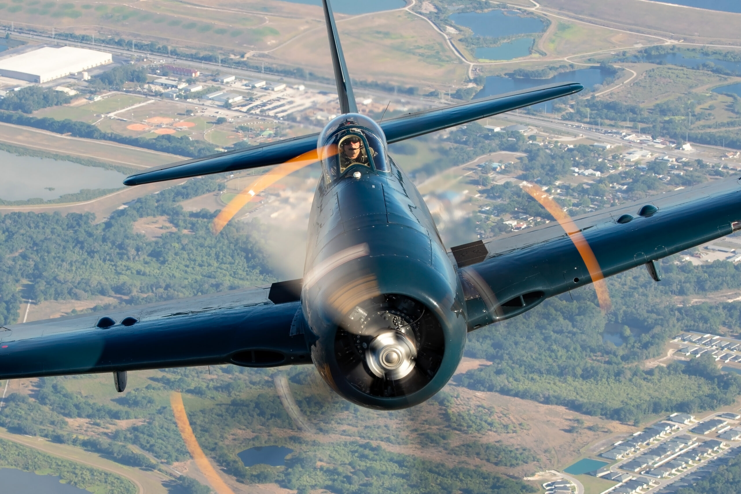 Head-on close-up of a Grumman F8F-1B Bearcat with the pilot clearly visible and propeller blurred