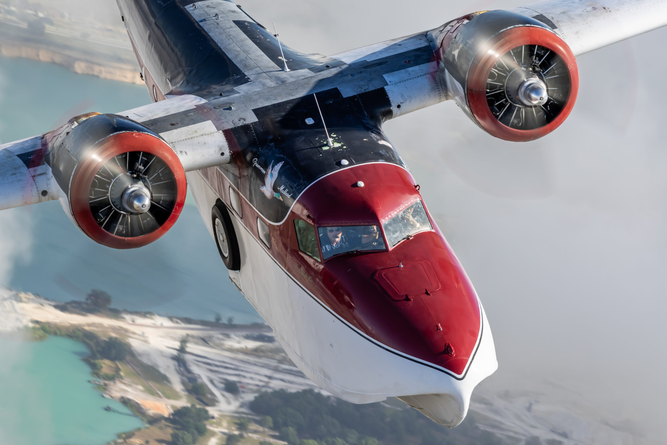 Close-up of Grumman G-73 Mallard flying boat in red, white and black with both radial engines turning and pilots visible