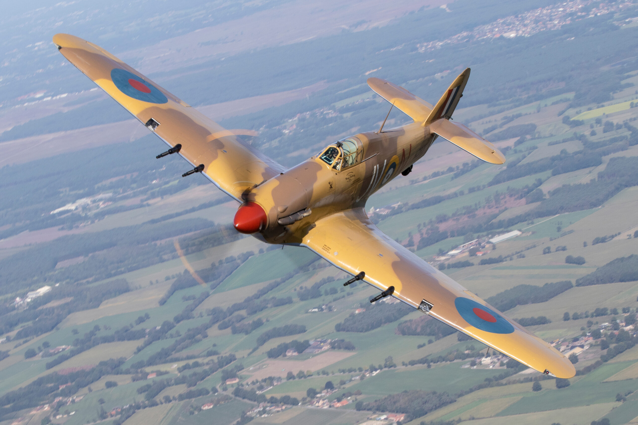 Hawker Hurricane in desert camouflage banking over fields with its propeller blurred