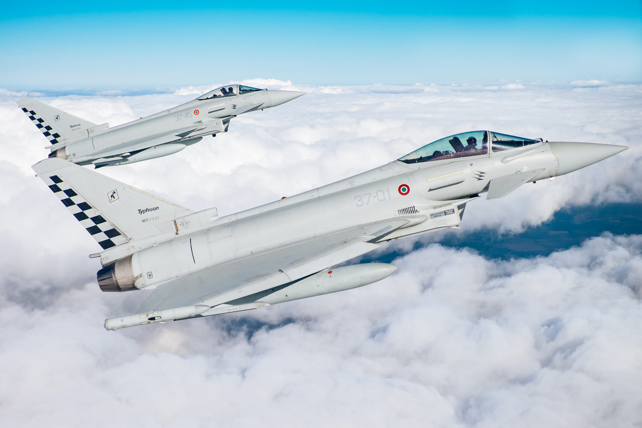 Two Italian Air Force Eurofighter Typhoons, 37-01 and 37-45 with checkerboard tails, in tight formation above a cloud deck