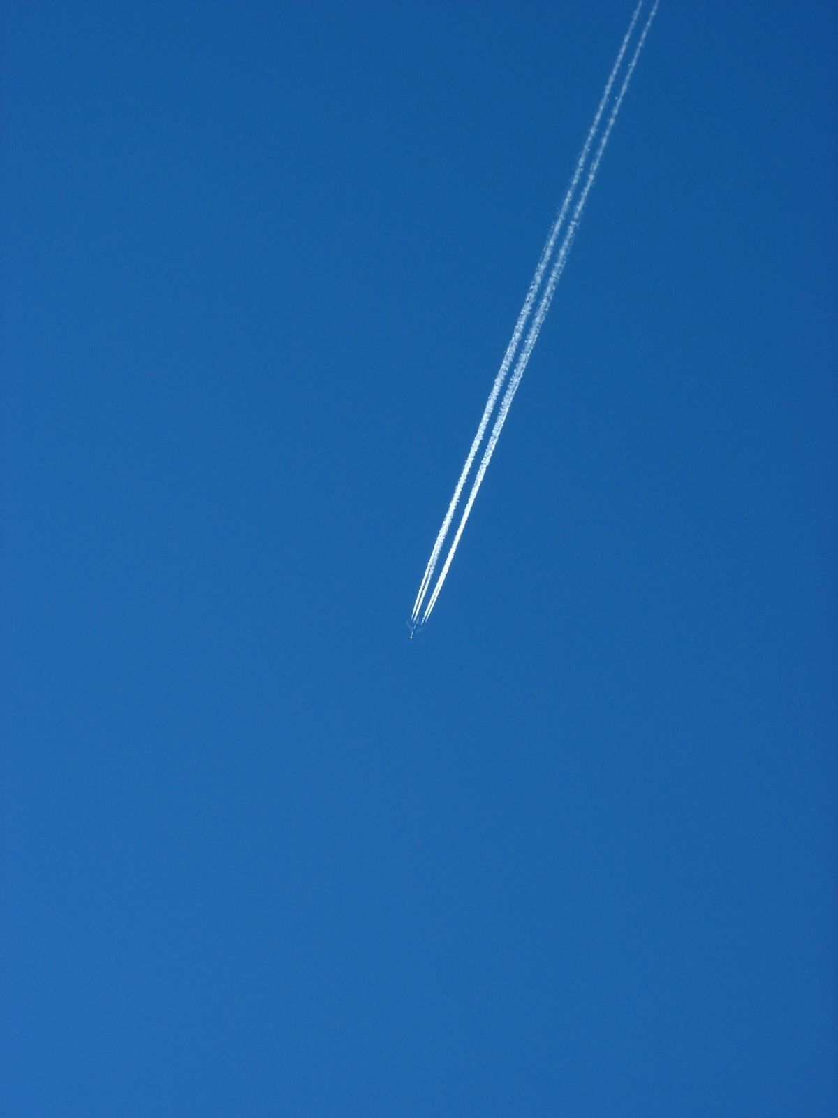 A single white jet condensation trail across a clear blue sky