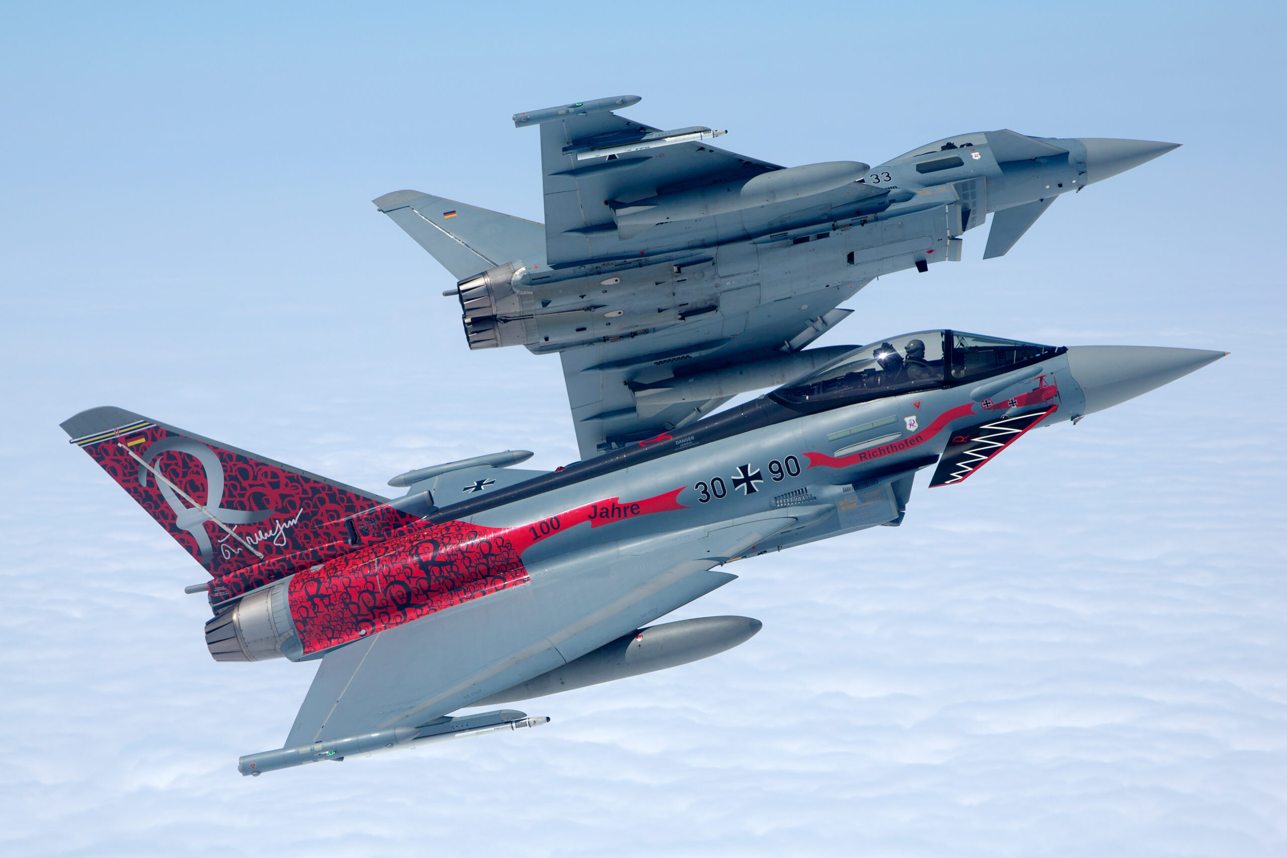 Two Luftwaffe Typhoons stacked vertically during a formation peel-away over cloud, the lower jet in the red Richthofen special scheme and the upper showing its underside