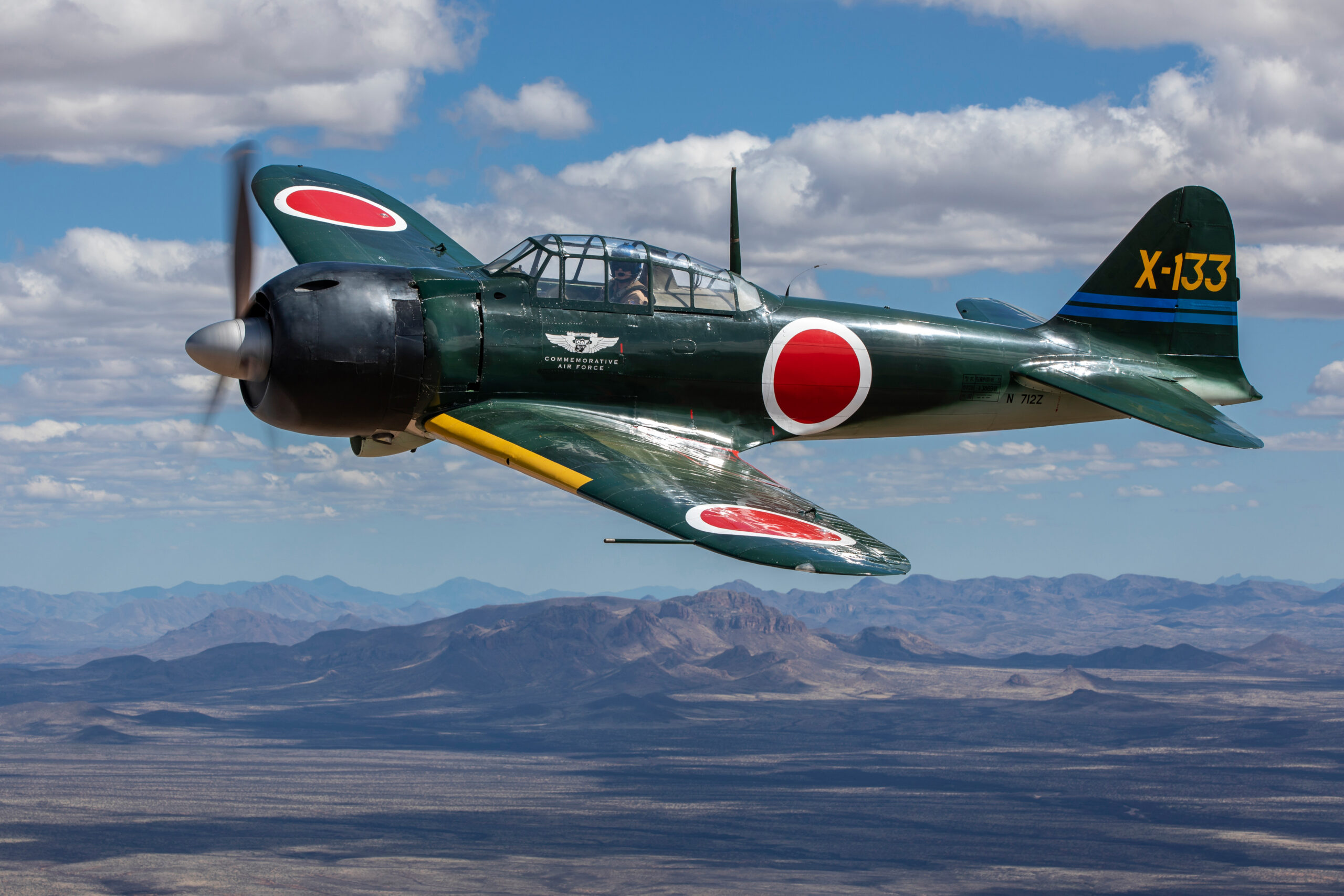 Dark green Mitsubishi A6M3 Zero with Japanese roundels and tail code X-133 flying over desert mountains