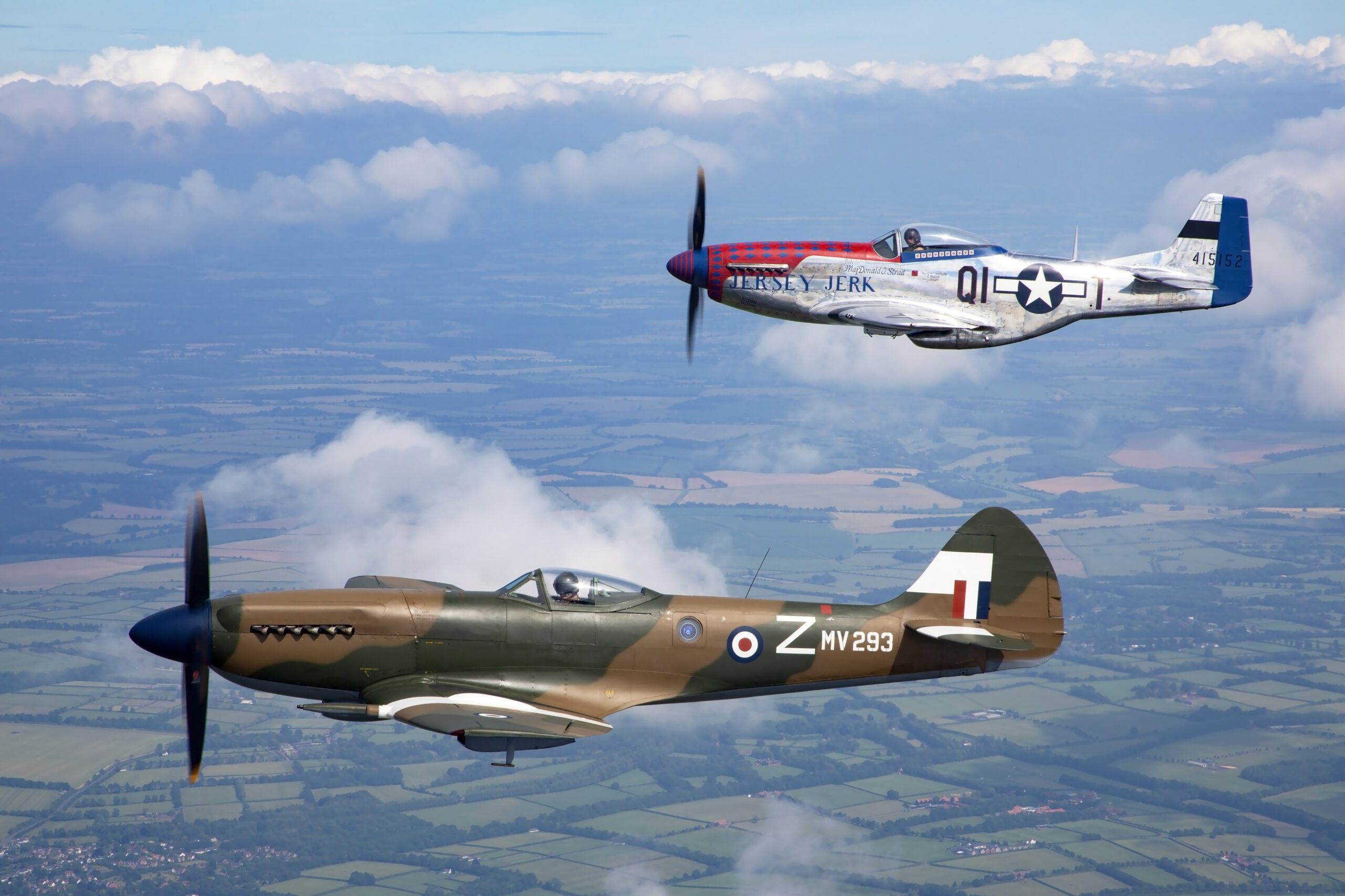 Mustang Jersey Jerk and camouflaged Spitfire MV293 both in perfect side profile with fully blurred propeller discs, flying over patchwork fields and cloud