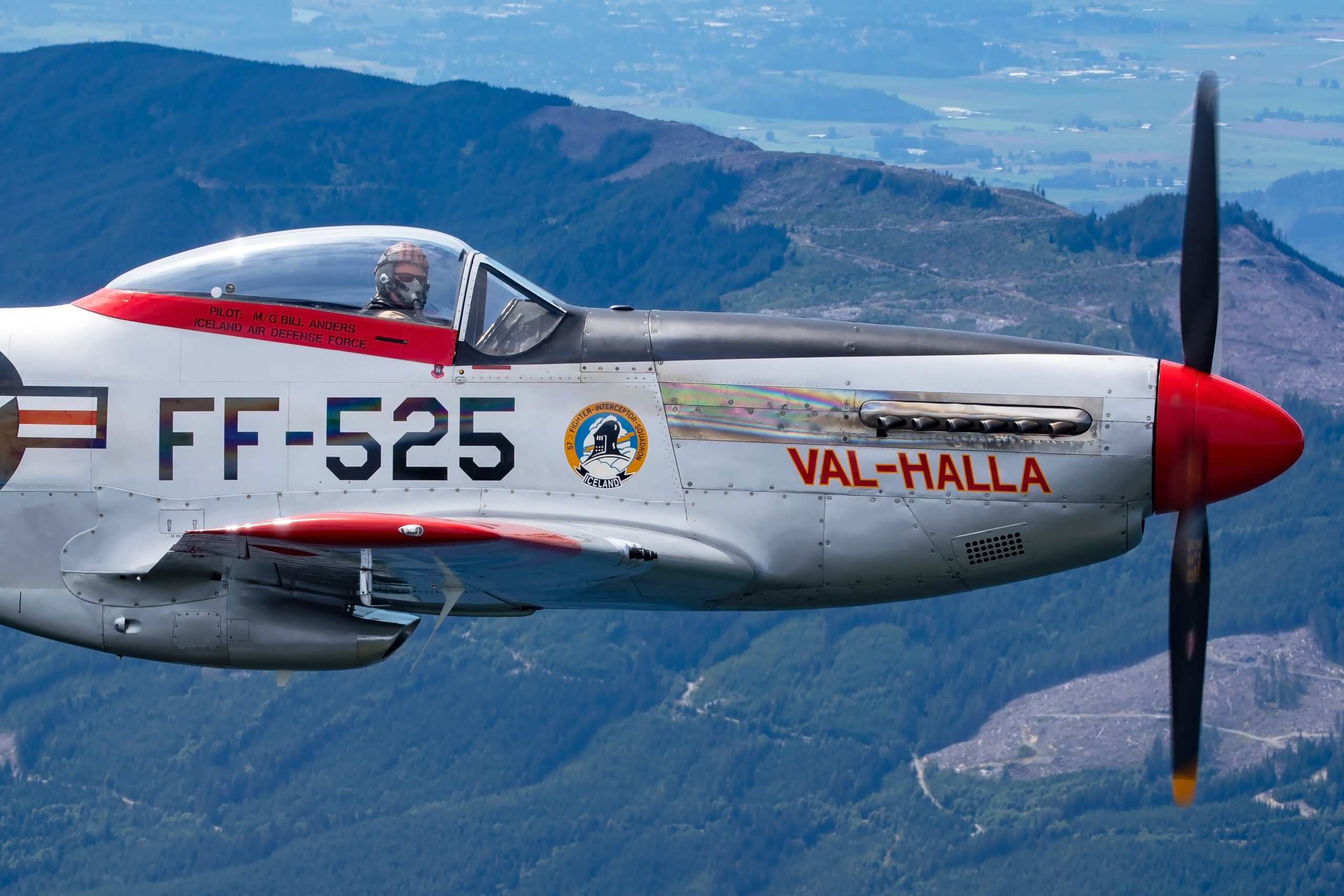 Close side profile of polished P-51D Mustang Val-Halla, code FF-525 with red nose and trim, pilot visible, mountains behind
