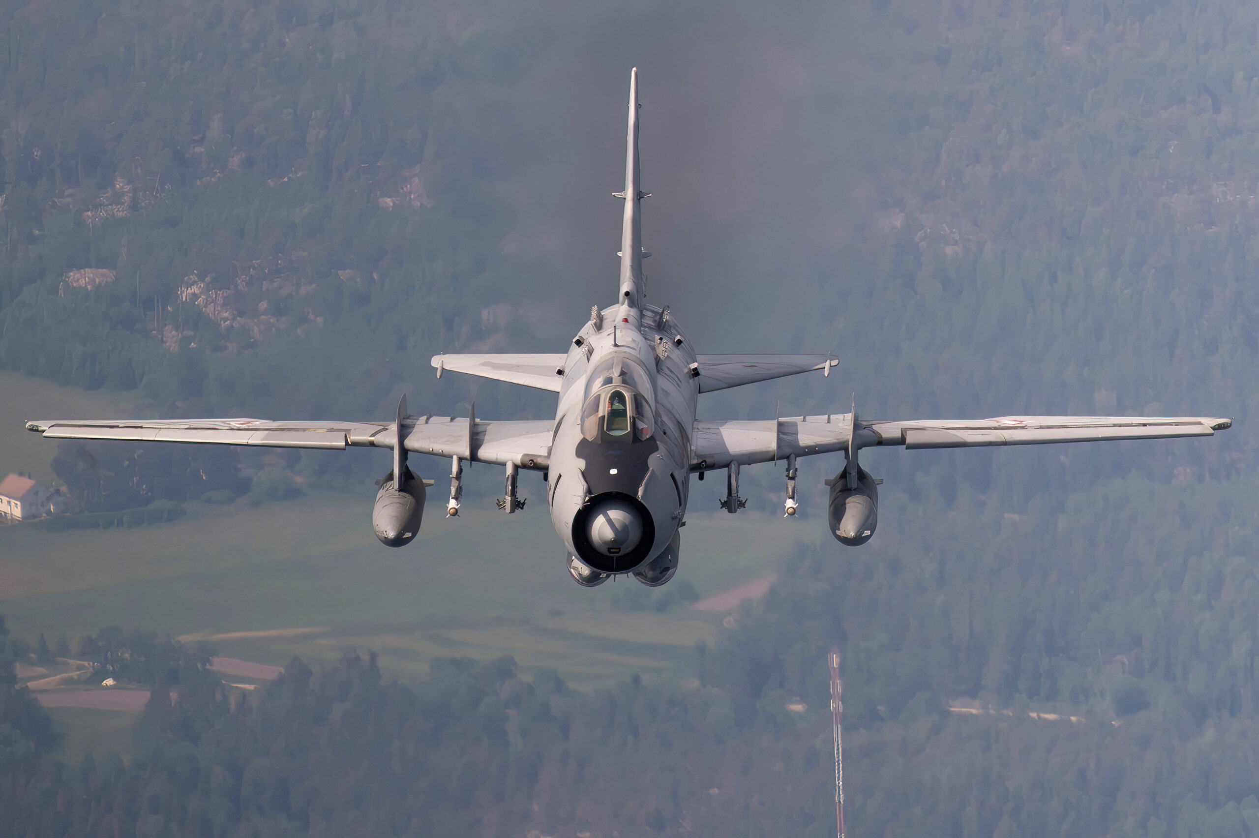 Polish Air Force Su-22M4 head-on with underwing fuel tanks, pilot visible in the cockpit, over forested terrain