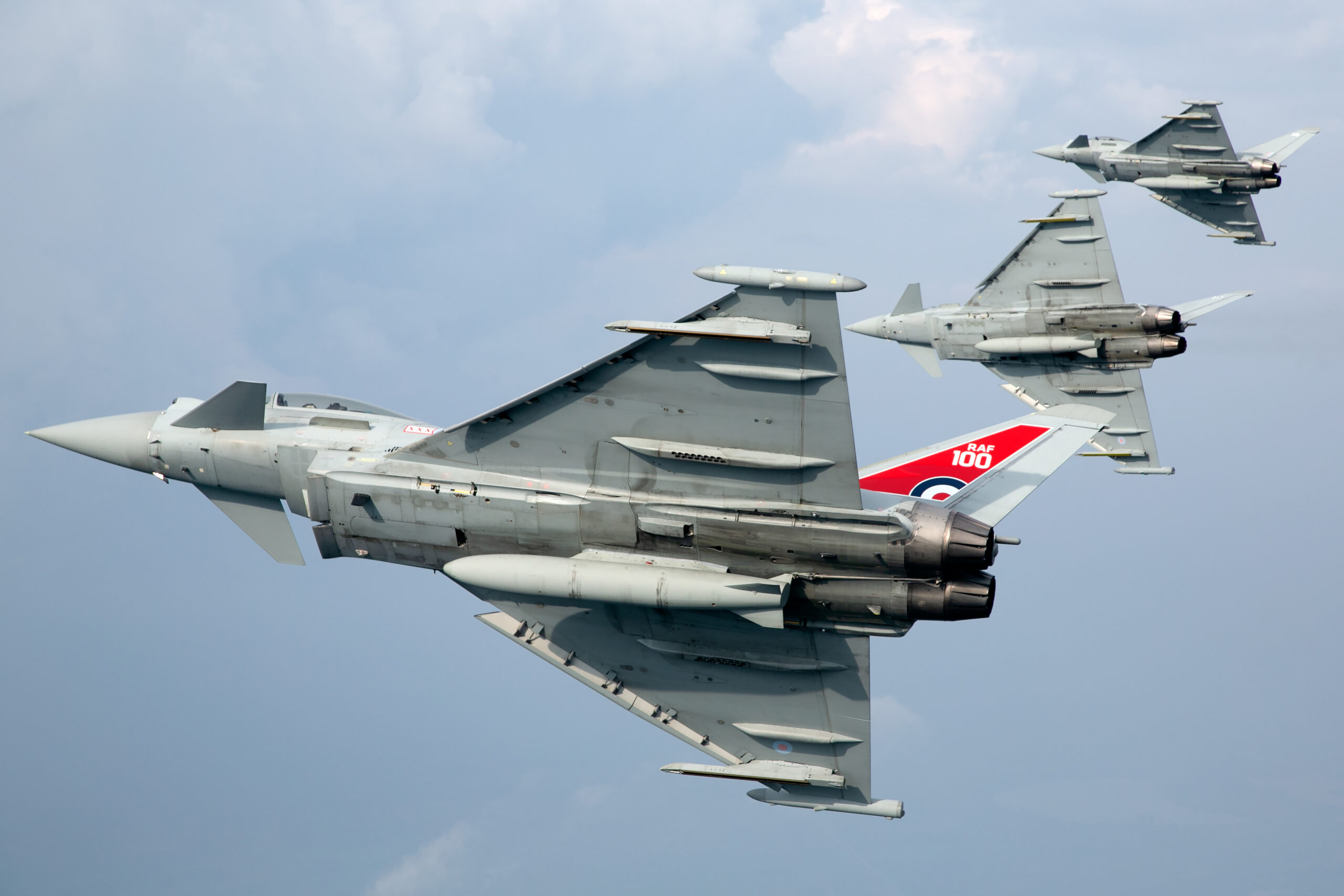 Three RAF Typhoon FGR4s banking away in stepped formation, the lead jet wearing the red-white-and-blue RAF100 centenary tail