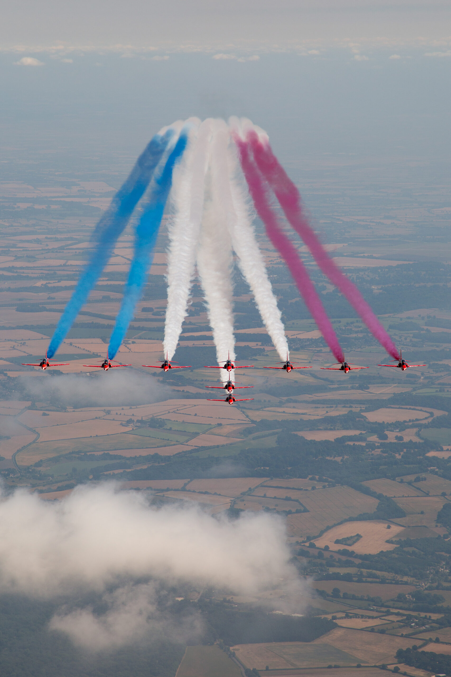 Red Arrows Hawk T1 jets in stepped formation trailing white smoke over countryside