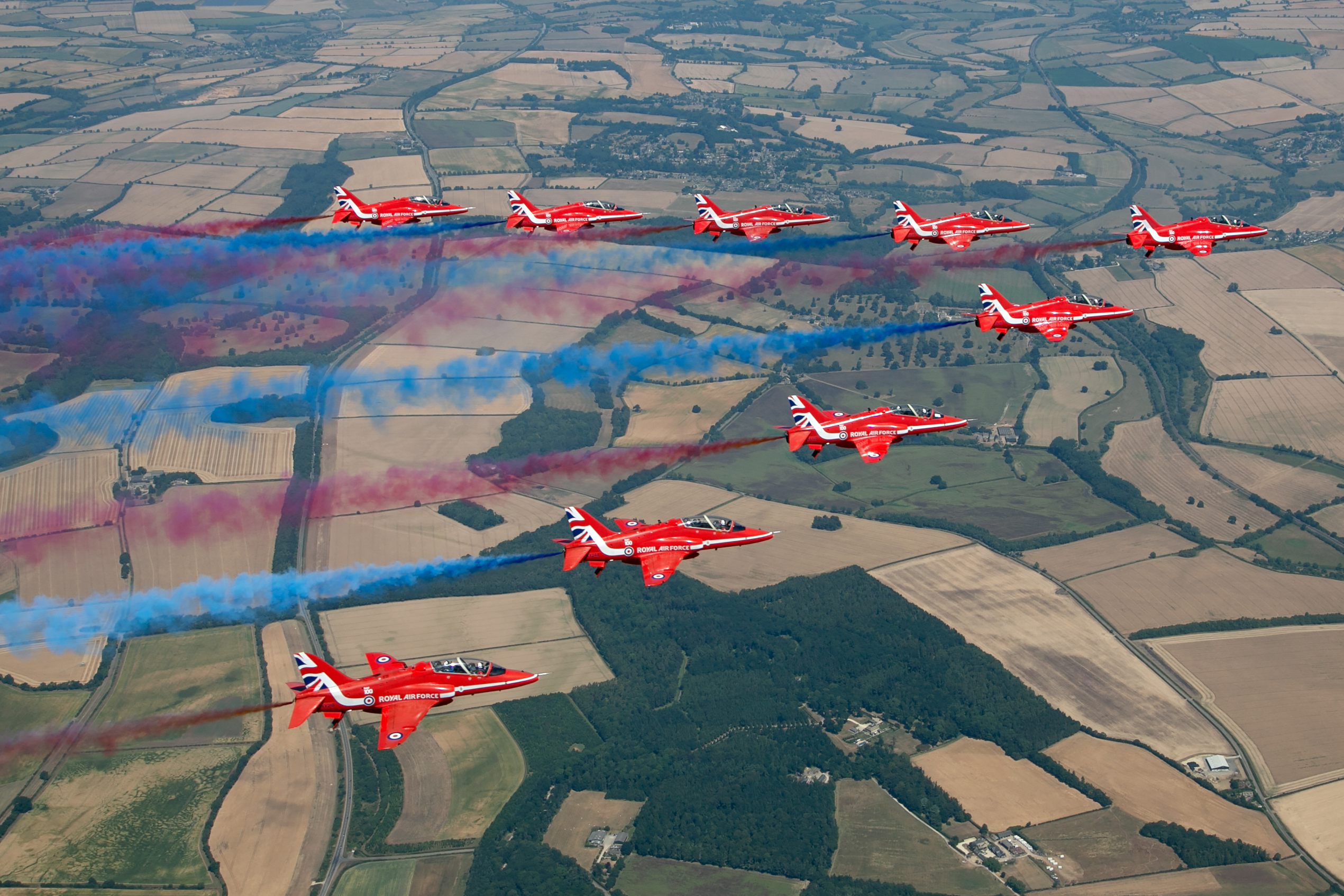 Red Arrows Hawk T1 formation trailing red white and blue smoke over countryside, air to air