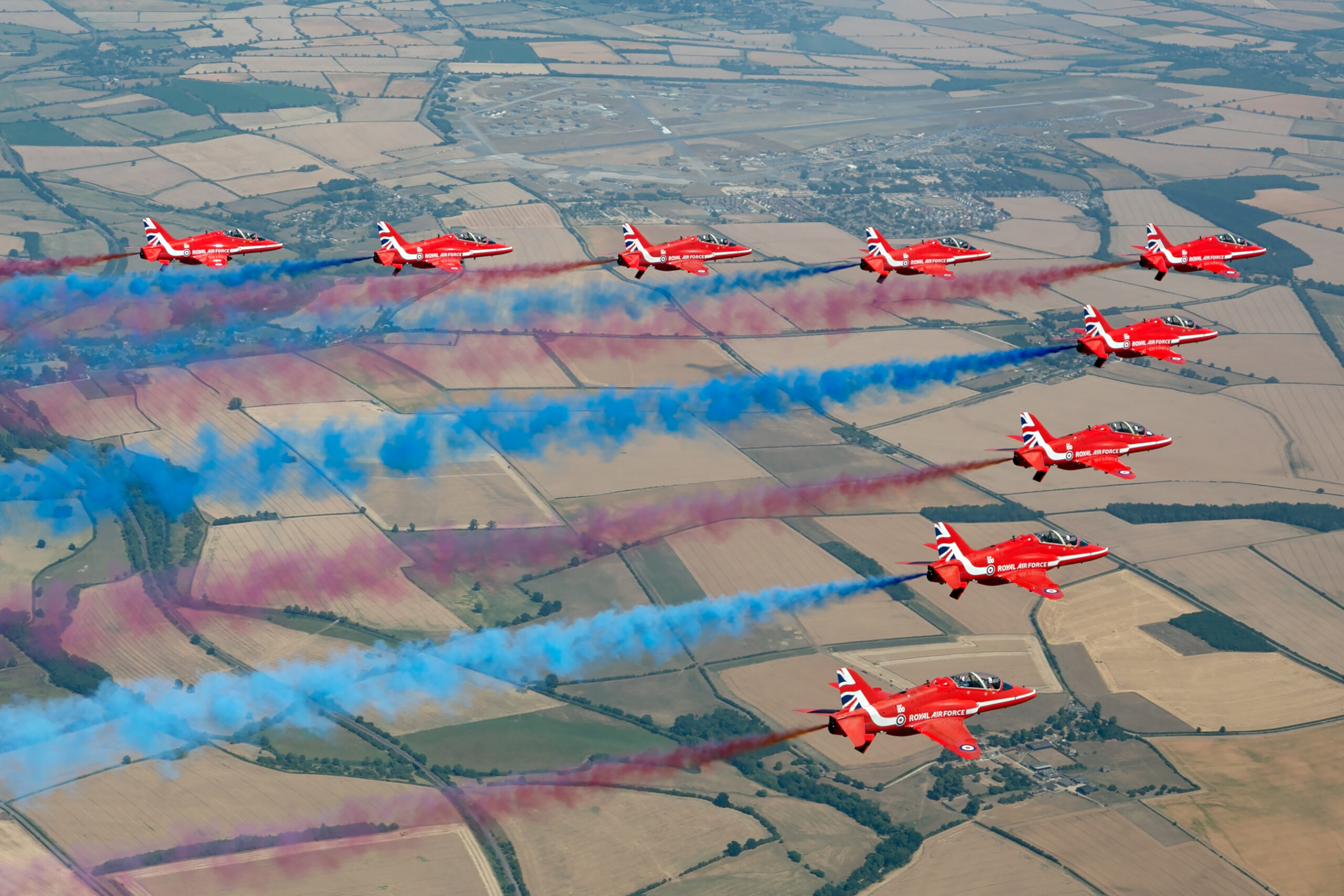 Nine Red Arrows Hawks from above trailing red and blue smoke over farmland