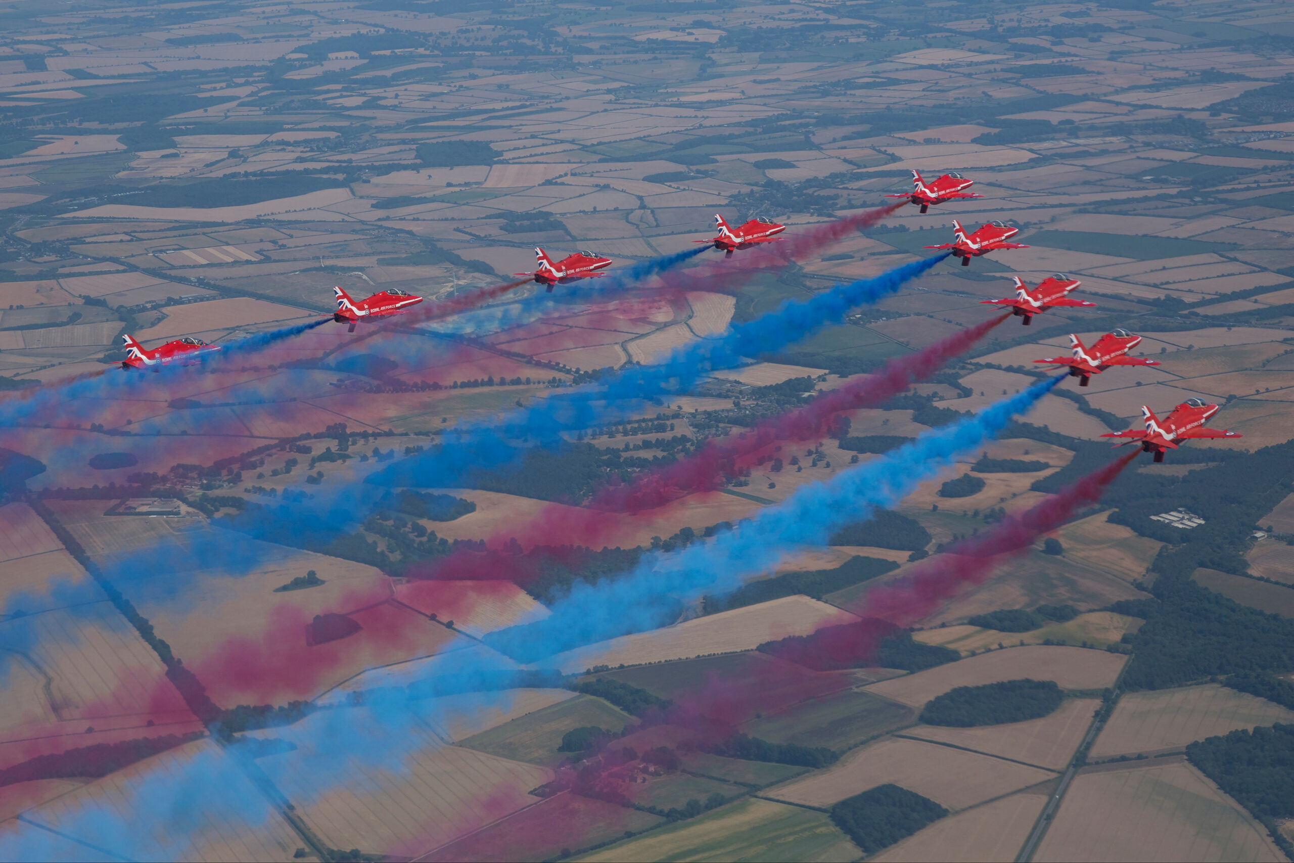 Royal Air Force Red Arrows Hawk T1s in nine-ship formation trailing red white and blue smoke, air to air