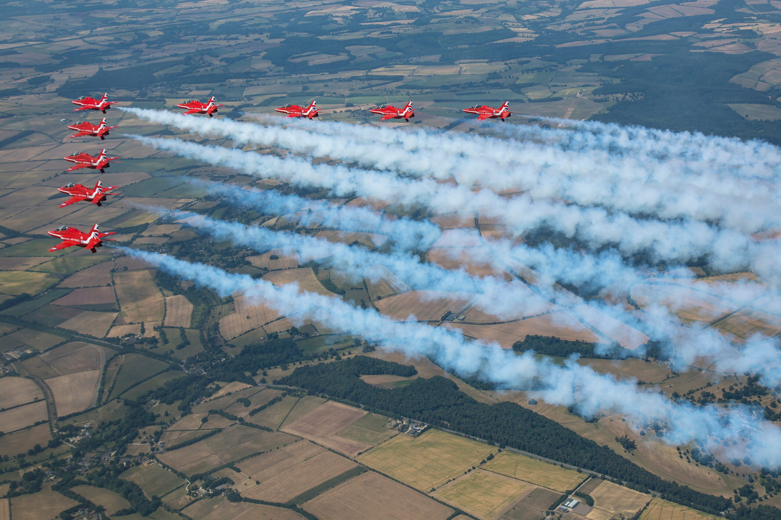 Red Arrows nine-ship formation trailing smoke over summer fields, air to air