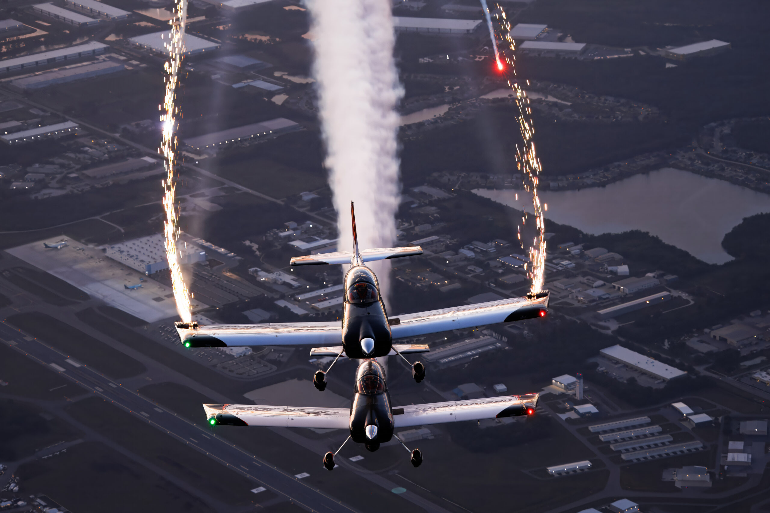 Two Van's RV-8s of the Redline team trailing wingtip sparklers at dusk over an airfield