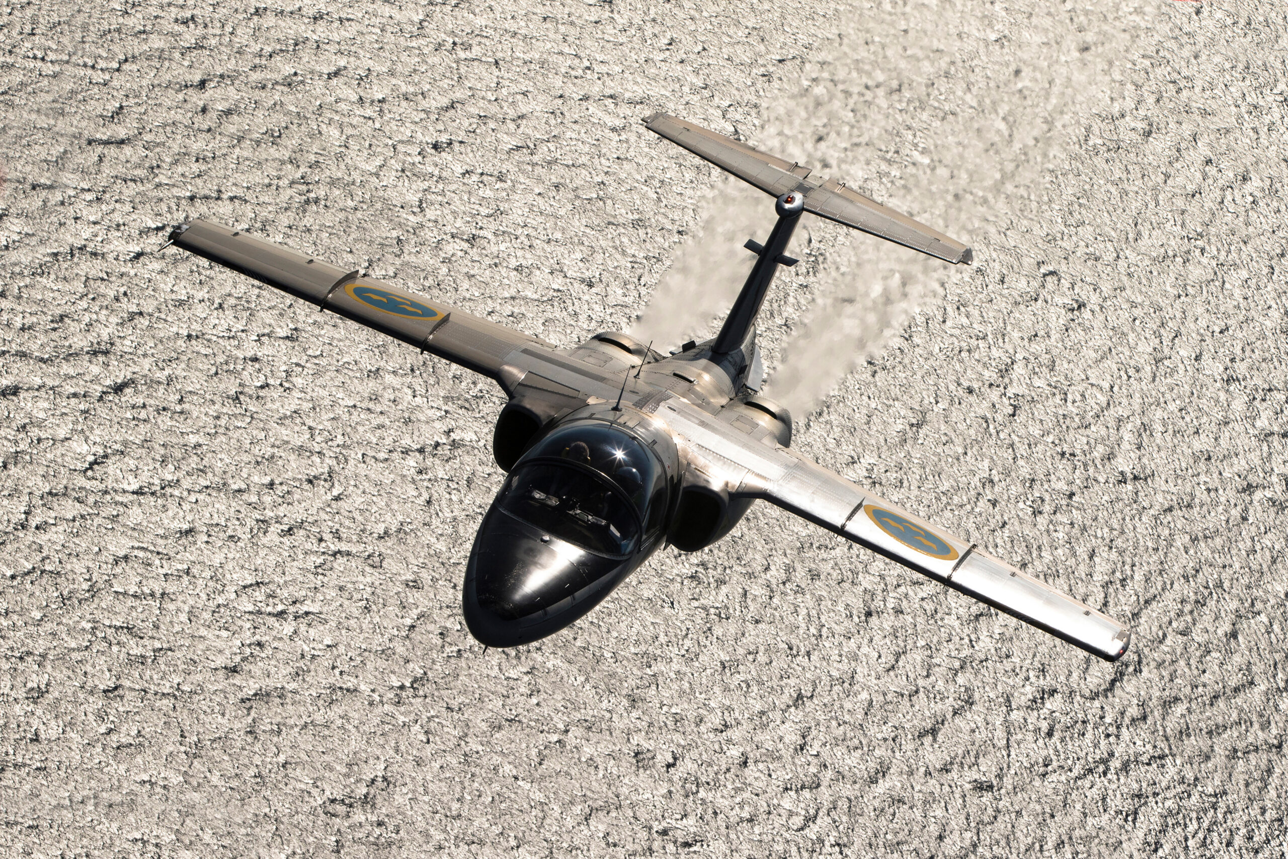 Saab SK 60B banking over a silver sun-glint sea