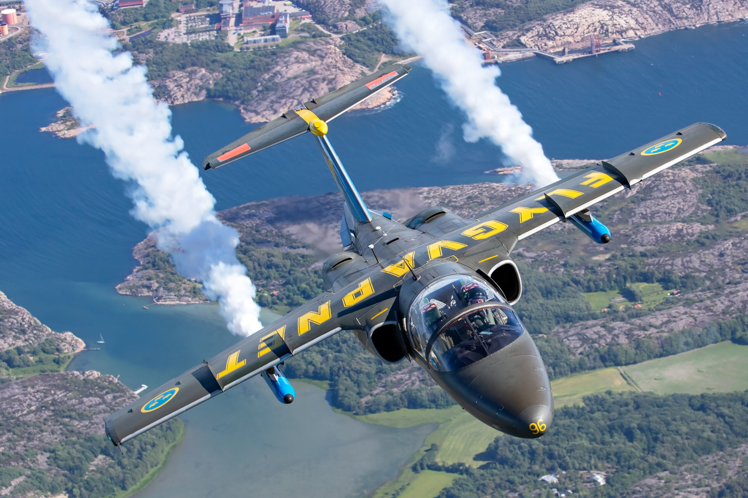 Saab Sk 60 in dark green with large yellow FLYGVAPNET titles, code 96 on the nose, diving towards a rocky coastline trailing smoke