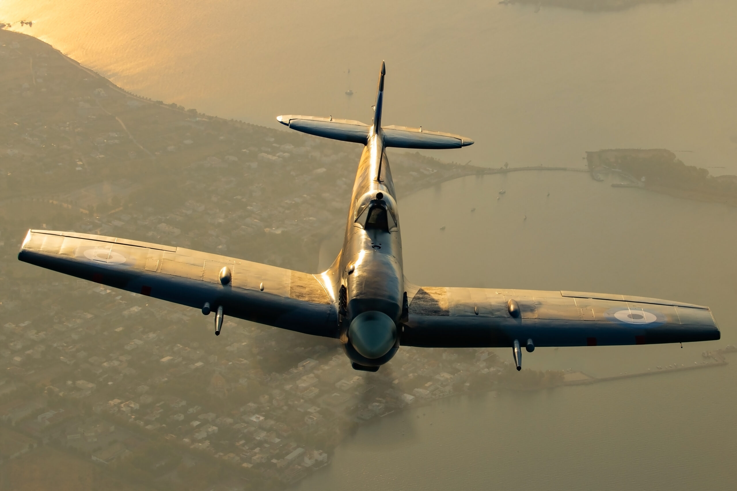 Supermarine Spitfire banking in warm dusk light over a coastline