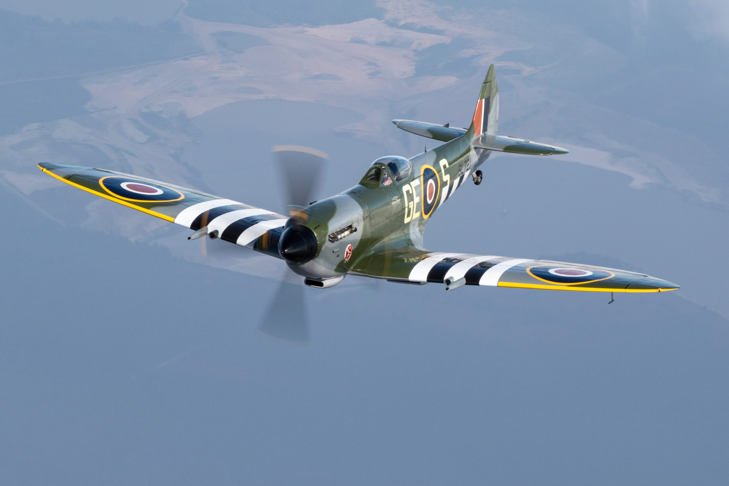 Supermarine Spitfire with D-Day stripes flying with its propeller blurred into an arc
