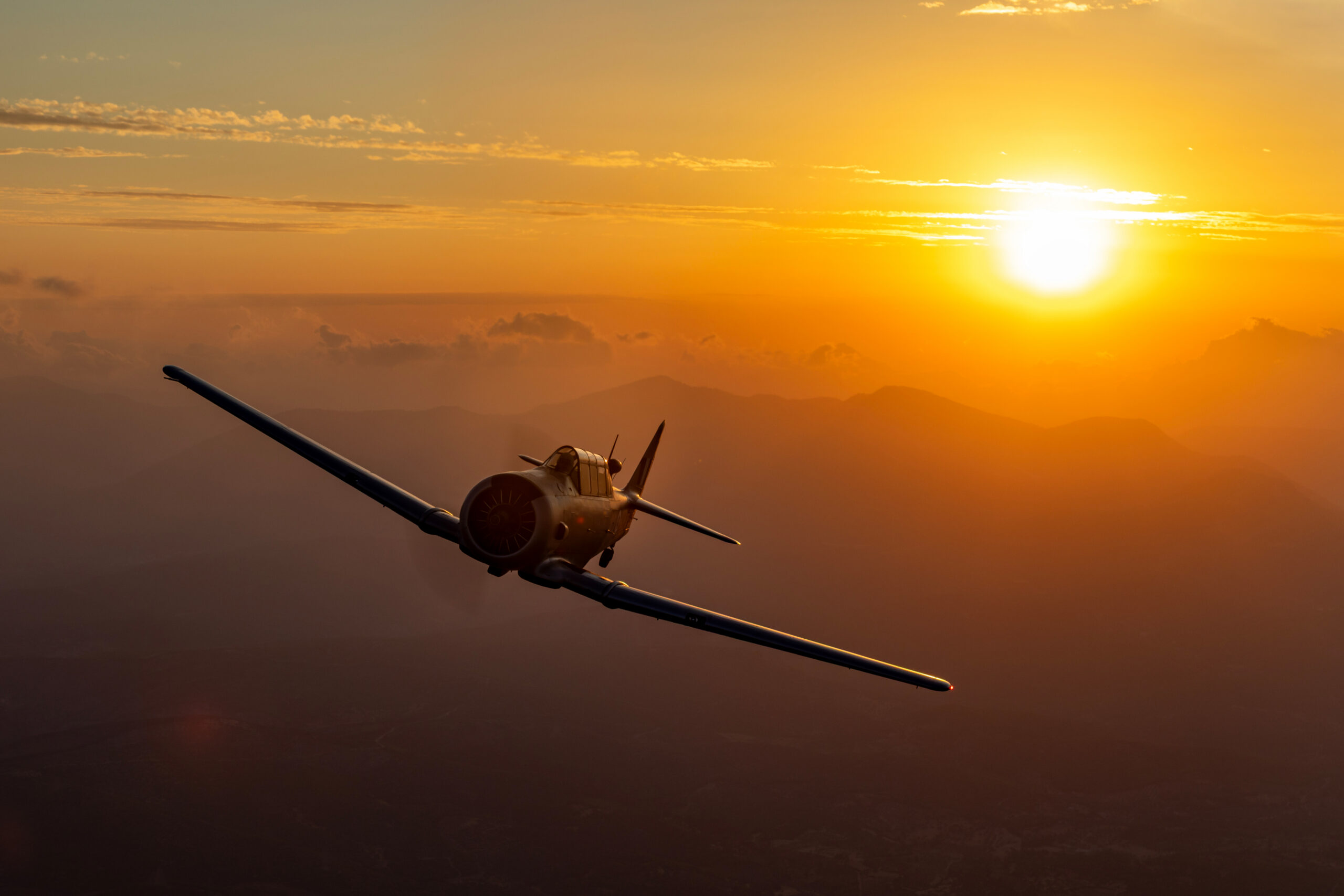 T-6G Texan flying towards the setting sun under an orange sky