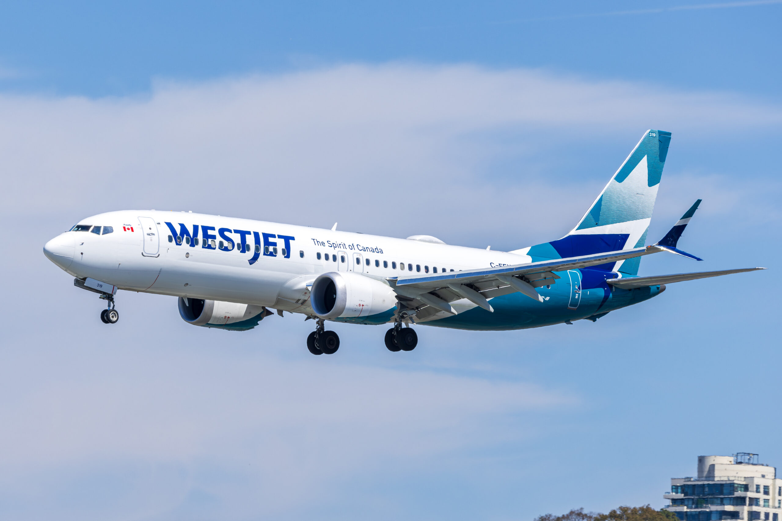 WestJet Boeing 737 MAX 8 C-FEWJ side-on with gear down on final approach, a high-rise building visible below