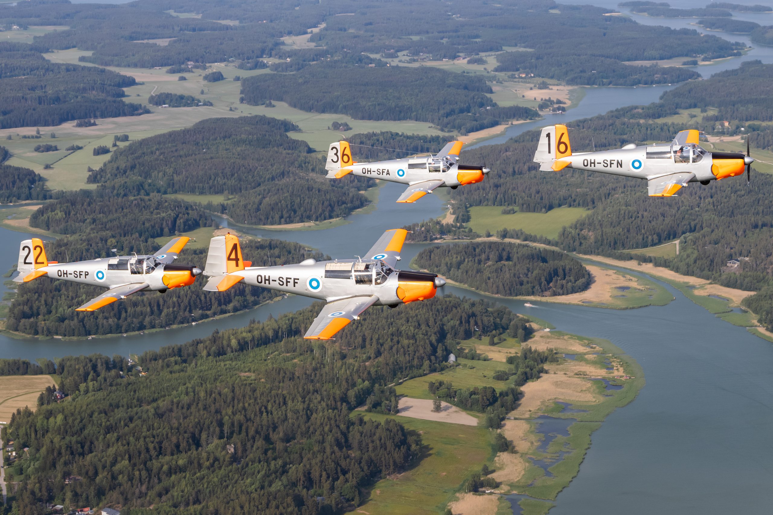 Four silver and orange Saab 91D Safirs of the Woikoski Safirs team in formation over Finnish lakes