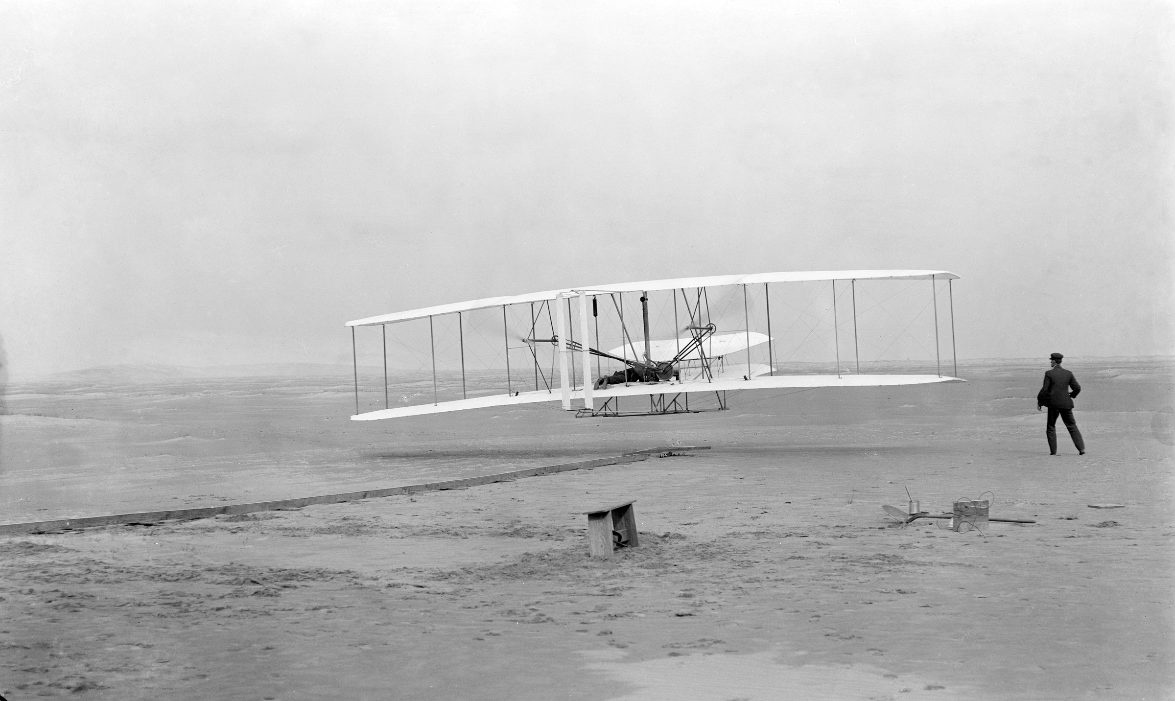 The Wright Flyer lifts off on its first flight at Kill Devil Hills on 17 December 1903, Orville Wright at the controls and Wilbur running alongside