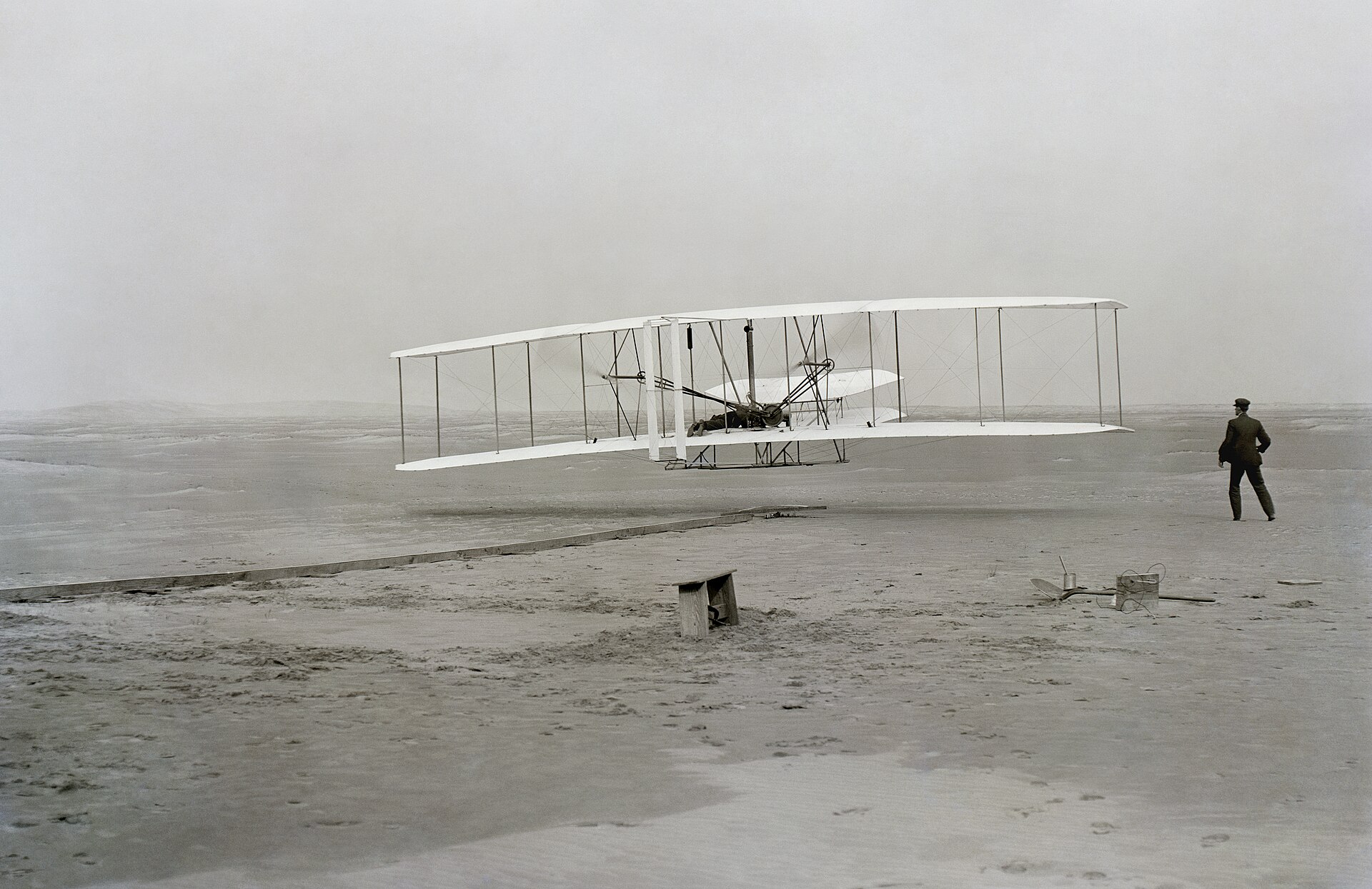 The Wright Flyer leaving the ground on its first powered flight at Kill Devil Hills on 17 December 1903, with Wilbur Wright running alongside