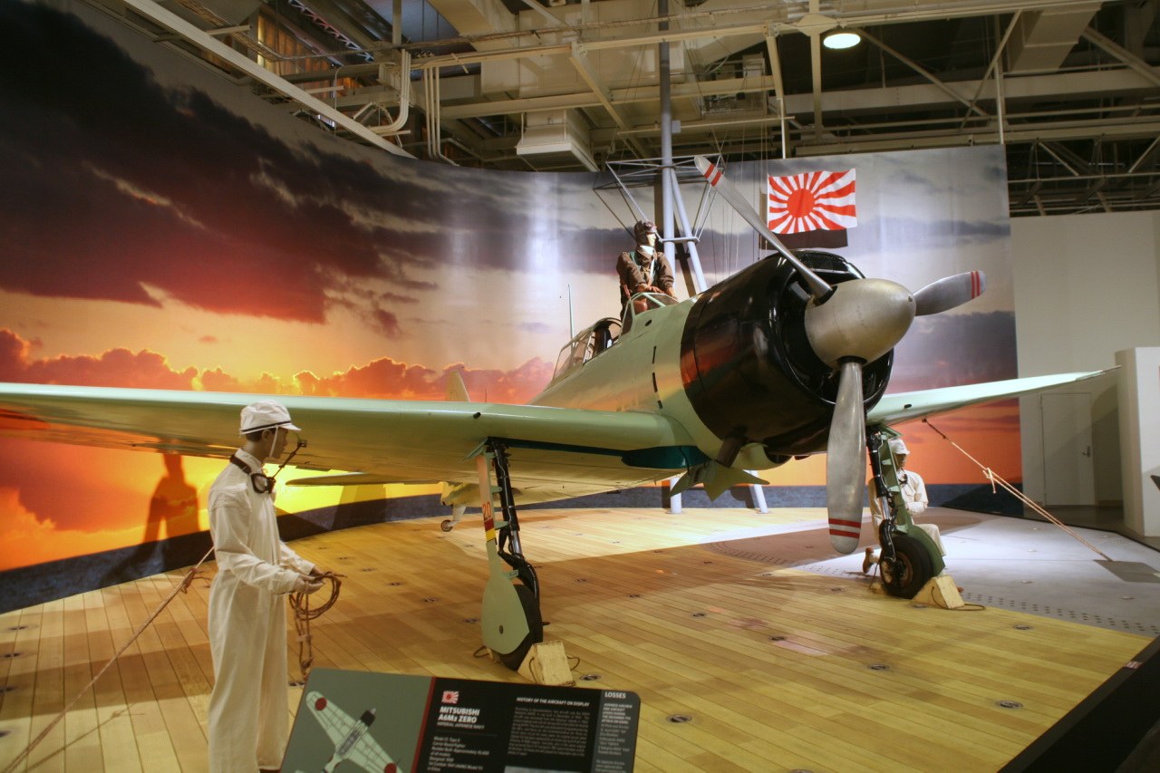 Restored Mitsubishi A6M2 Zero on a mock carrier deck inside a museum hangar at Ford Island