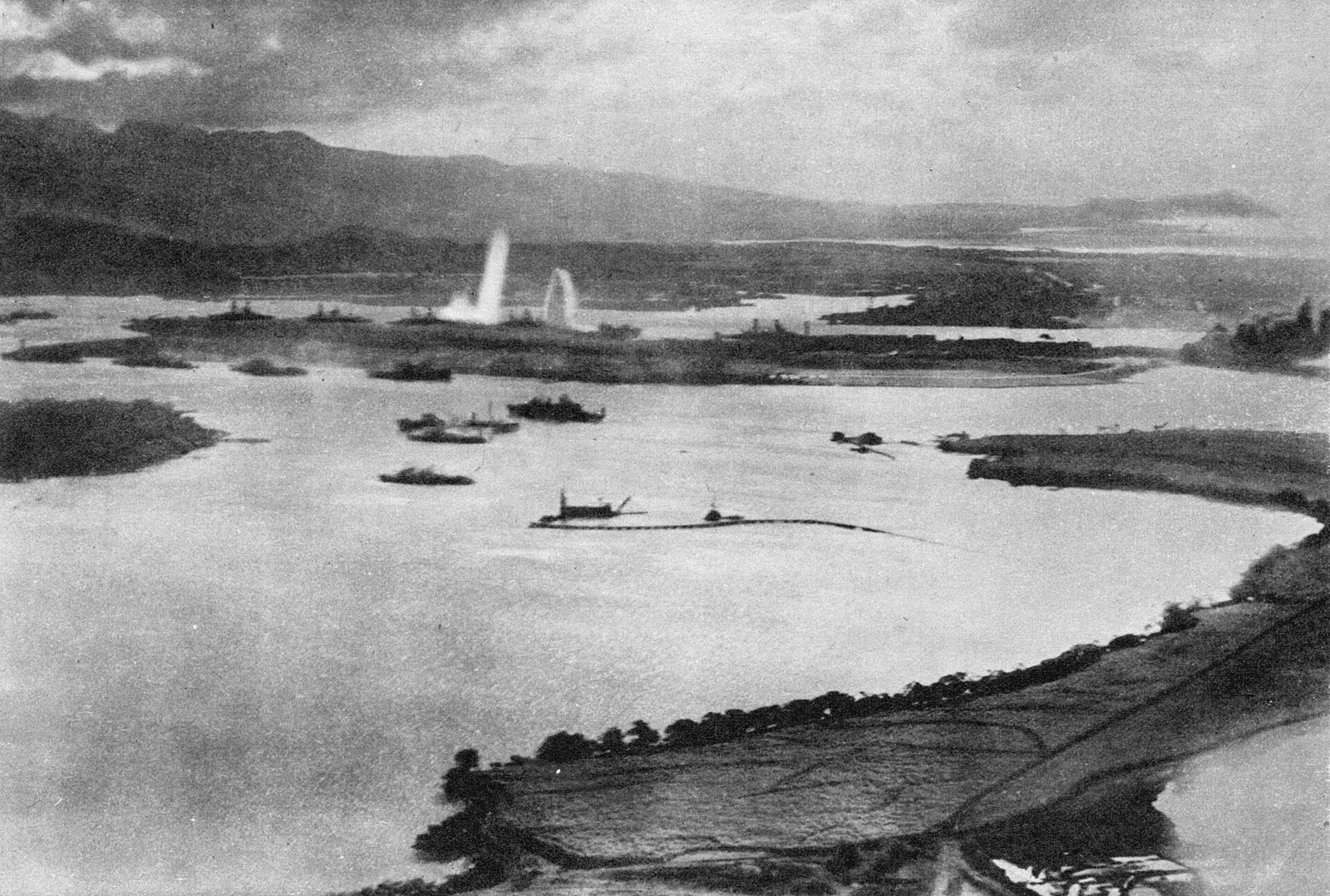 Oblique aerial photograph across Pearl Harbor during the attack showing torpedo water columns