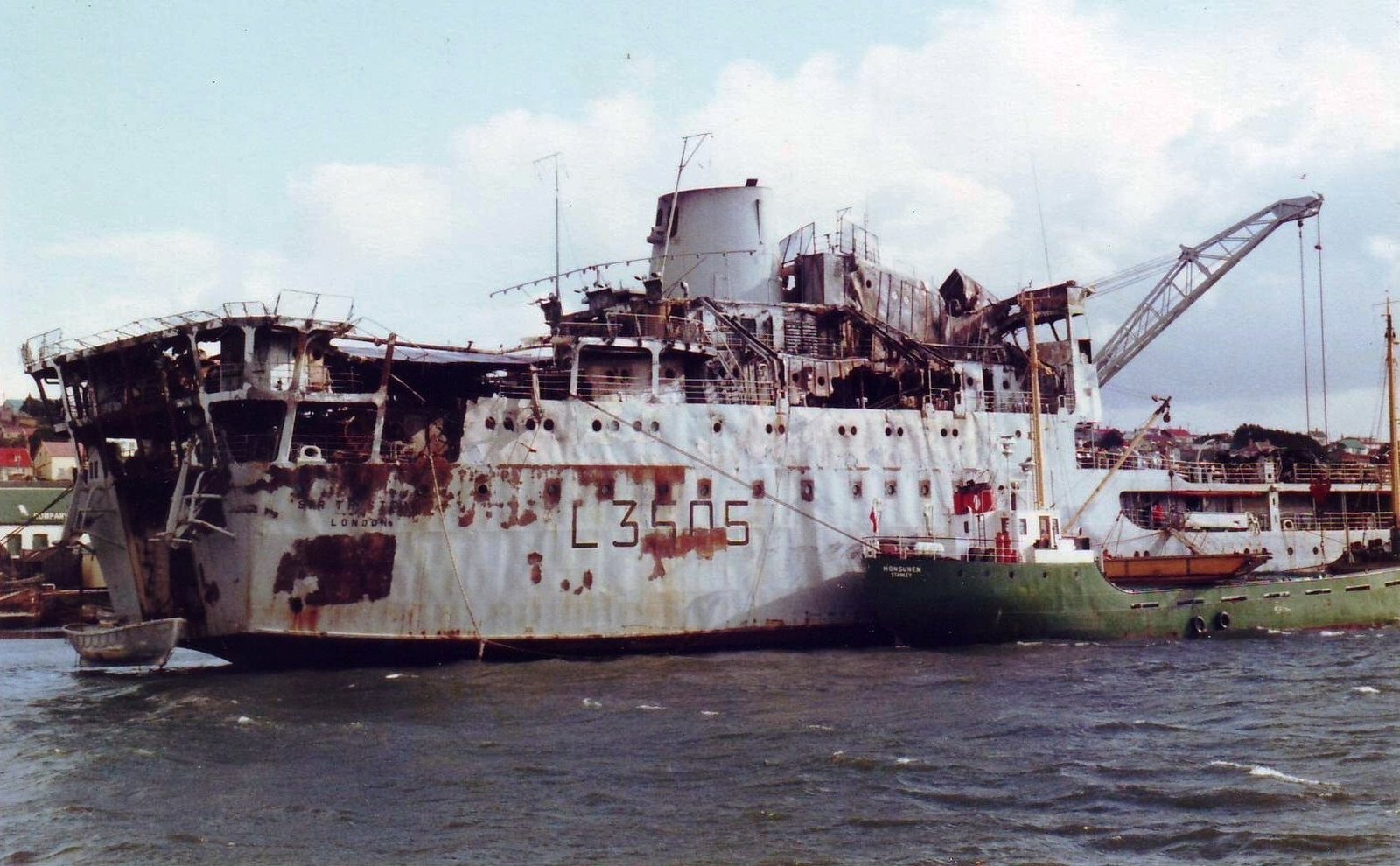 The burnt out hull of RFA Sir Tristram, pennant L3505, lying at Port Stanley with a crane alongside