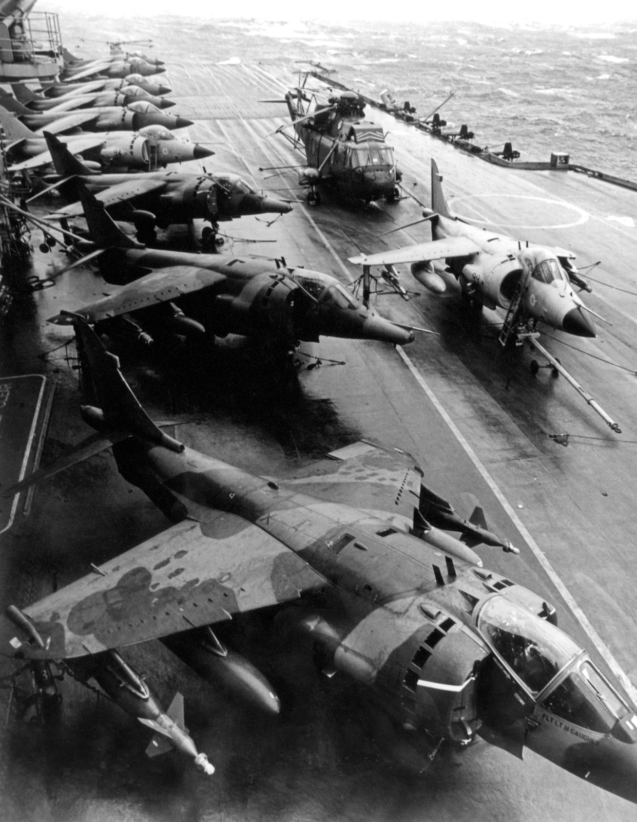 Sea Harriers, camouflaged Harrier GR3s and a Sea King ranged along the deck of HMS Hermes, photographed in 1982
